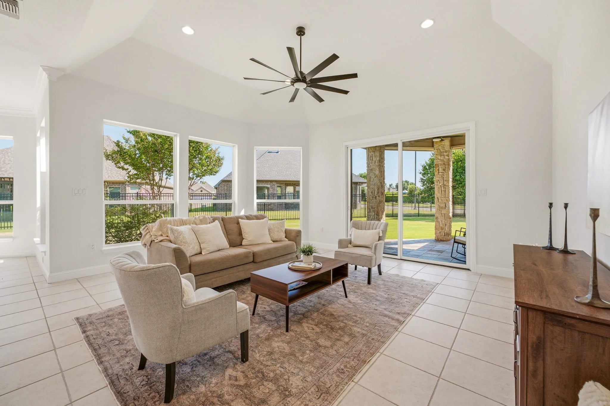 Spacious living area featuring high vaulted ceilings, recessed lighting, a modern ceiling fan, large windows, and tile flooring