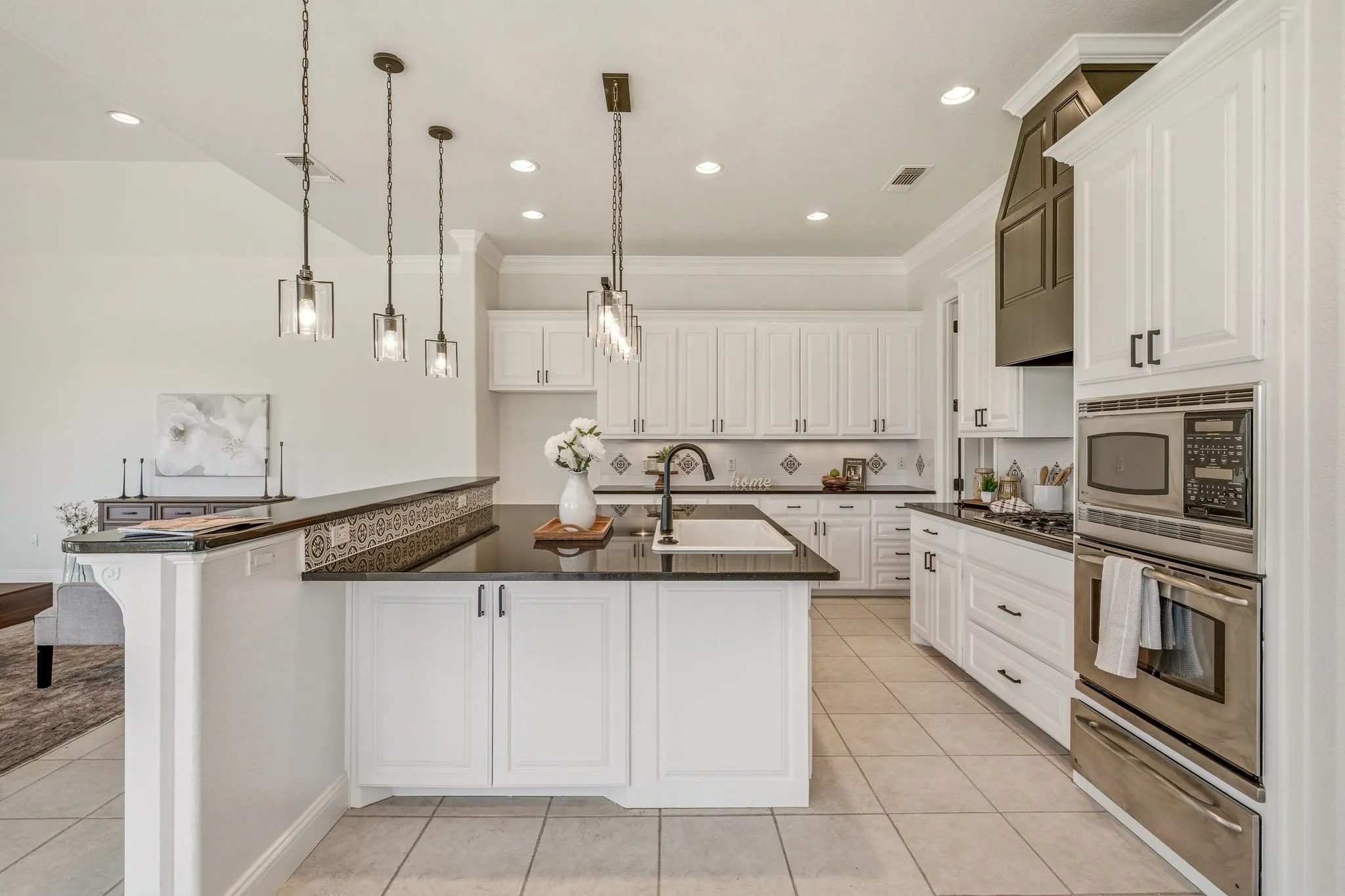 Spacious kitchen featuring white cabinetry, dark countertops, a central island with sink, a built-in oven and microwave, and a decorative tile backsplash