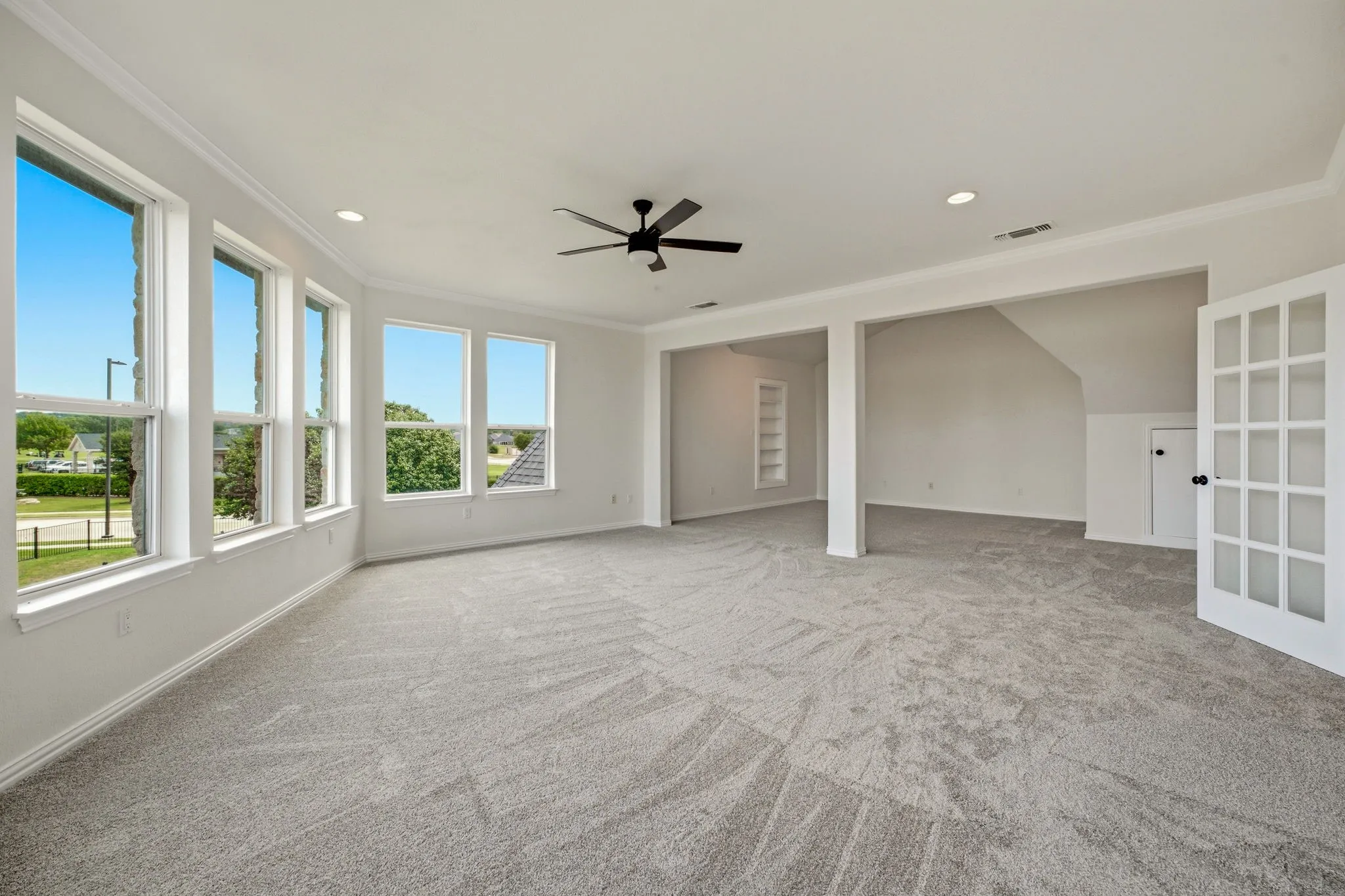 Spacious room with large windows, light gray carpeting, a ceiling fan, recessed lighting, and white French doors