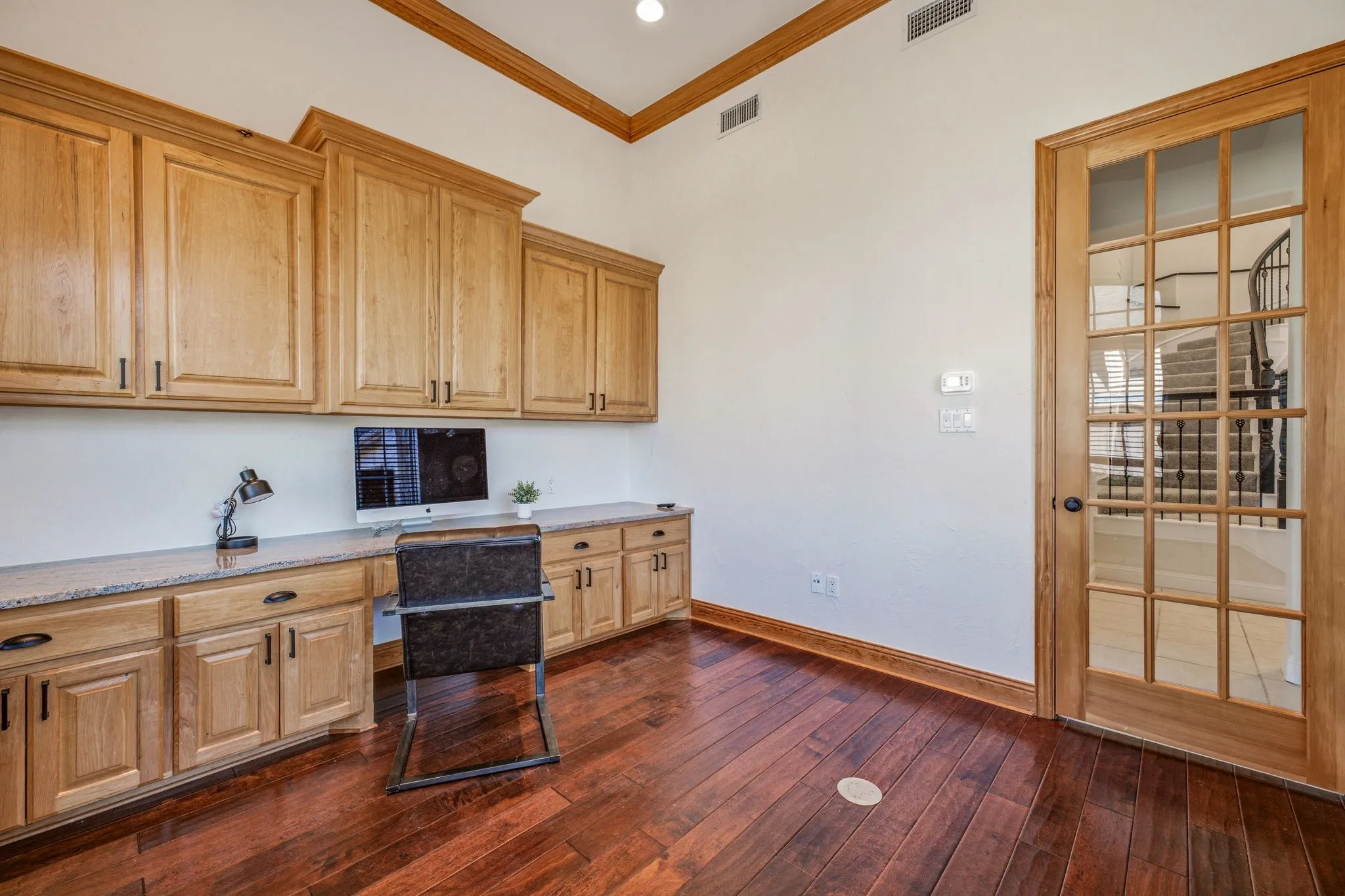 Dedicated office space featuring extensive built-in cabinetry, granite-style countertops, wood-finish flooring, and a glass-paned door