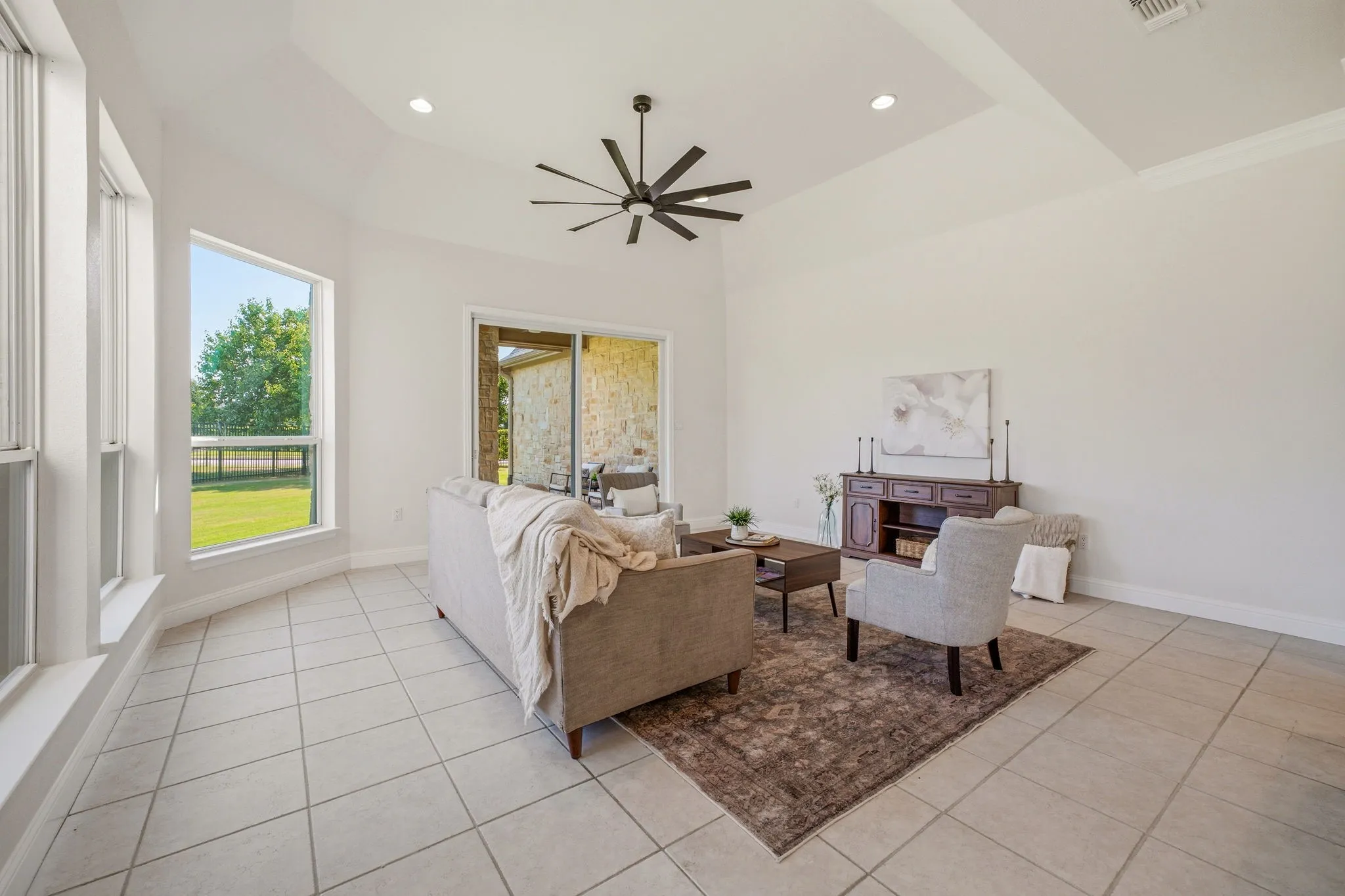 Spacious living area featuring light-toned tile flooring, large windows, a sliding glass door, a contemporary ceiling fan, and recessed lighting