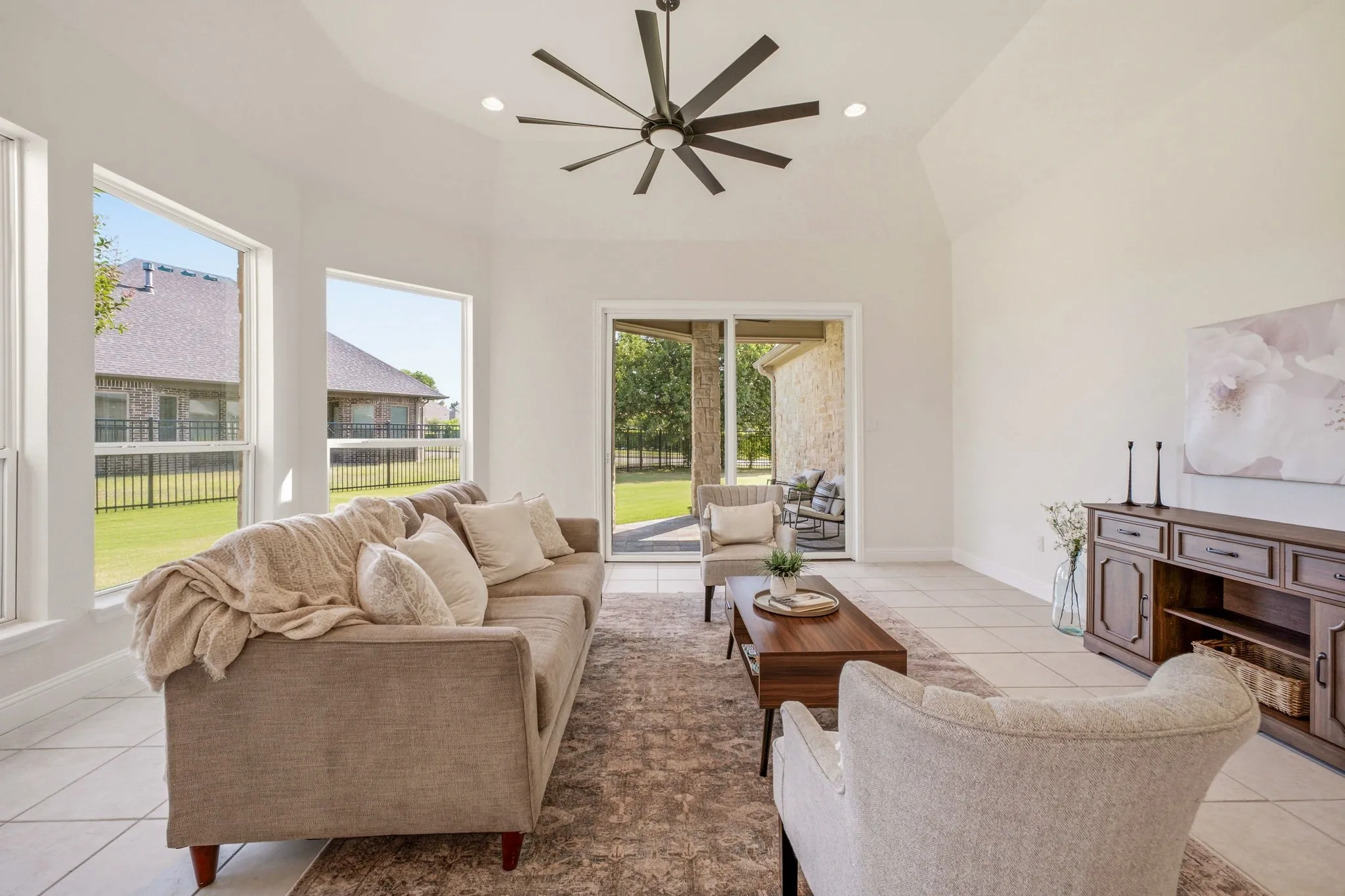 Spacious living area featuring large windows, a vaulted ceiling with a modern ceiling fan, and tile flooring