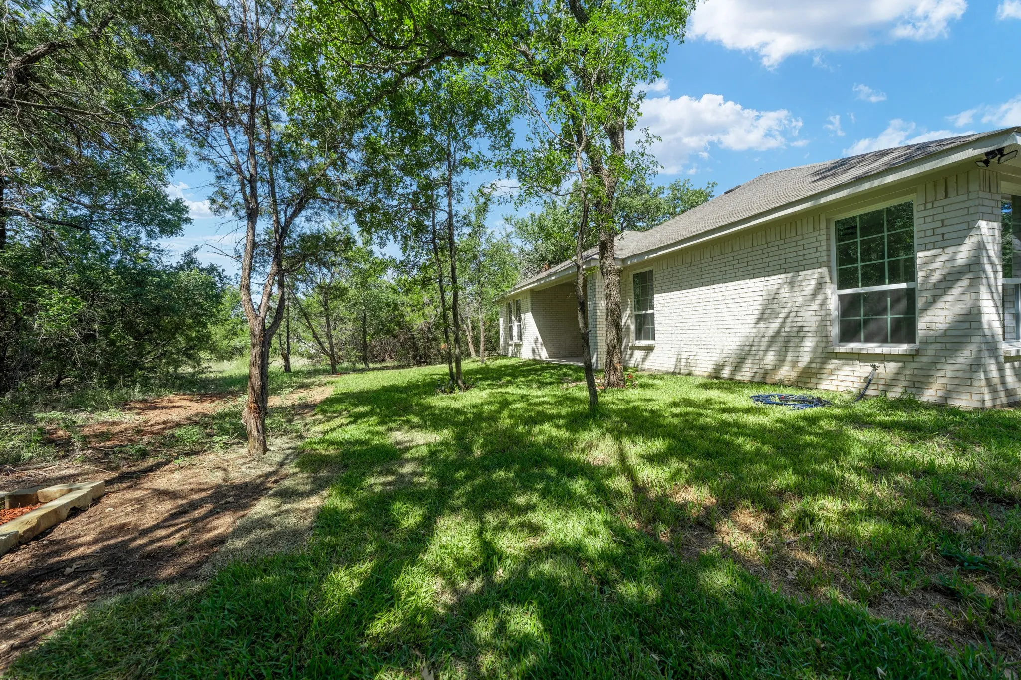 Exterior brick facade with multiple windows, surrounded by mature trees and a lawn