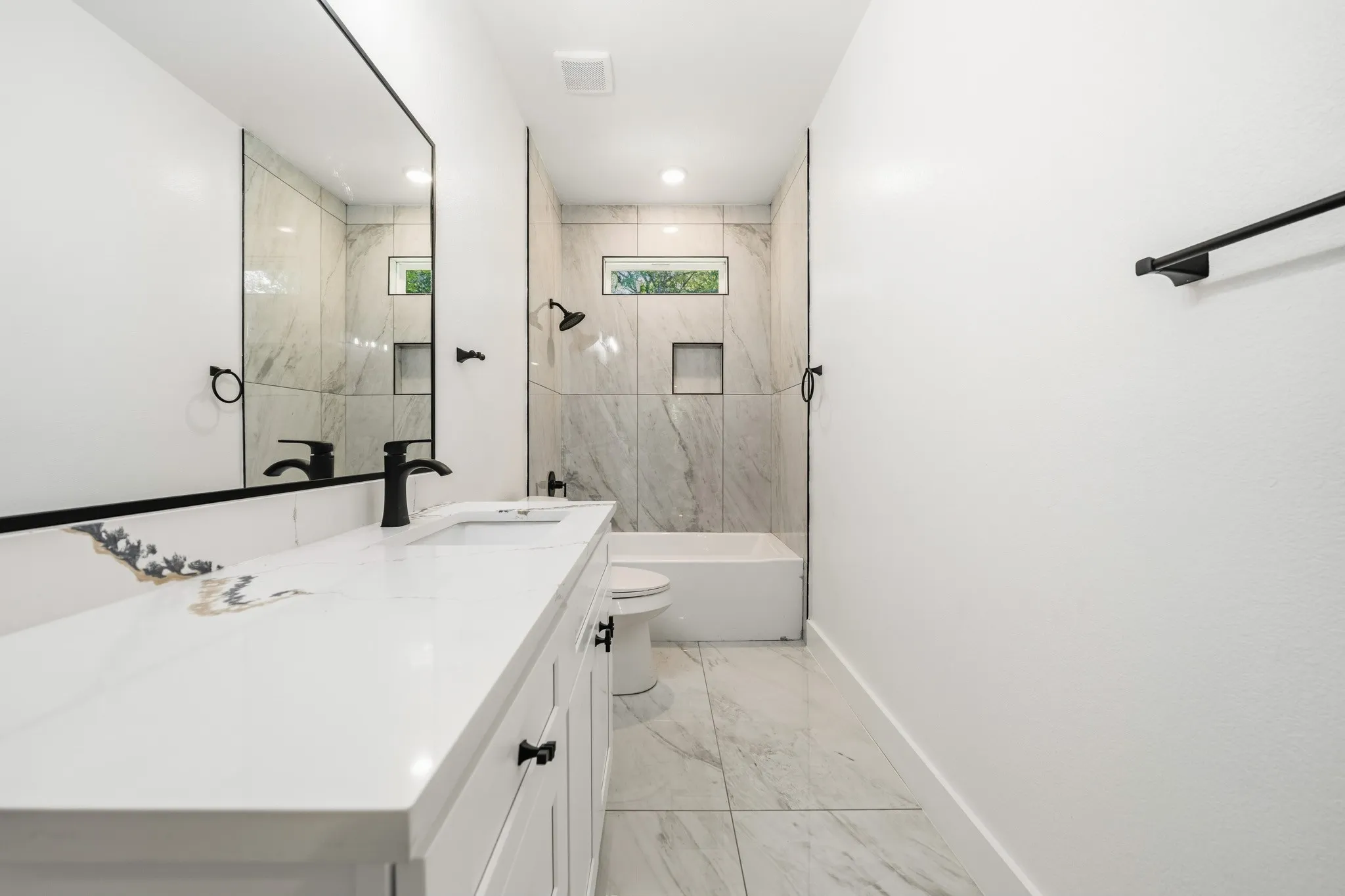 Bathroom featuring a white vanity with integrated sink, black fixtures, and a large mirror