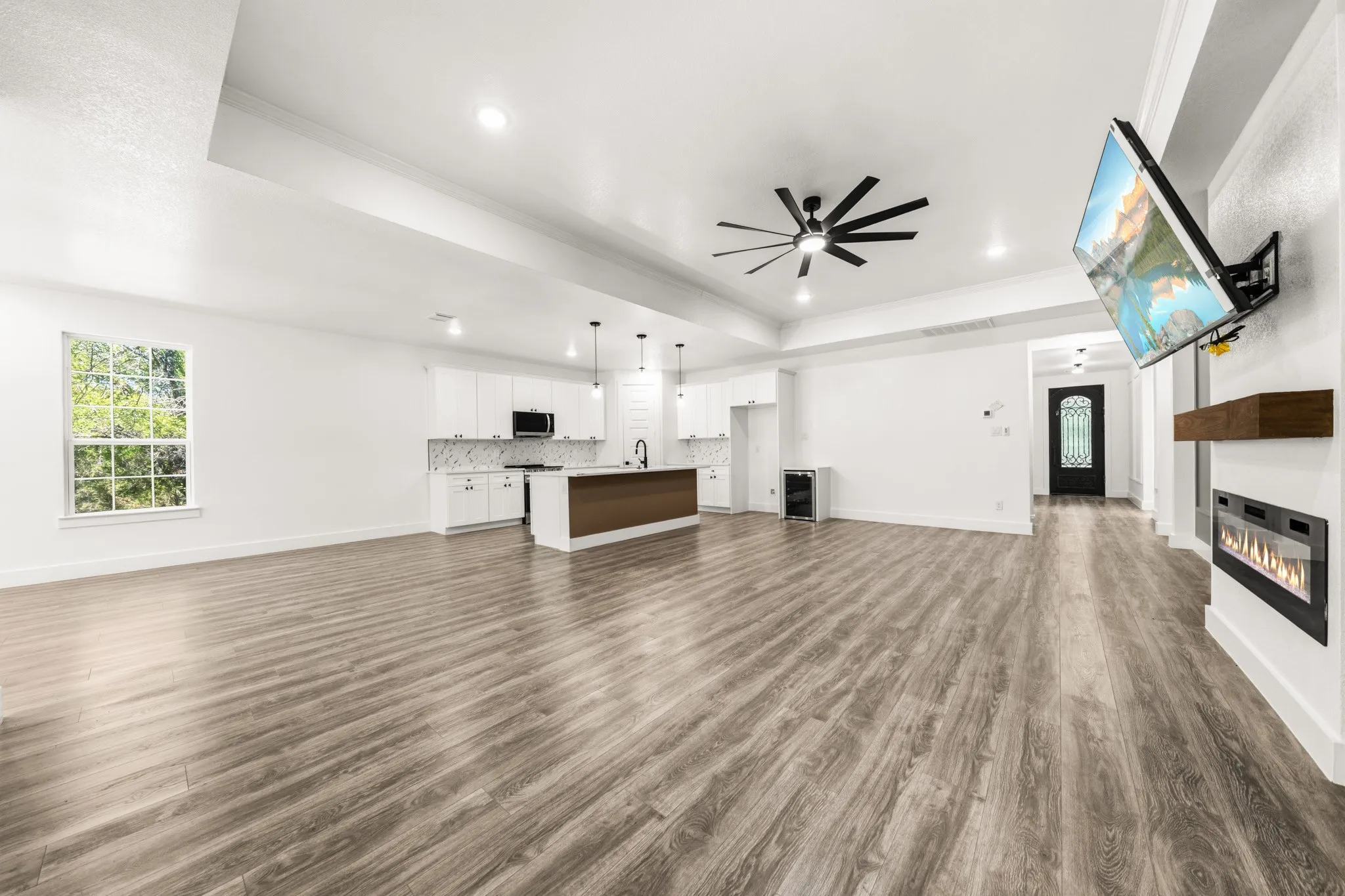 Spacious living area featuring wood-finish flooring, a contemporary fireplace with a wood mantle, and a modern ceiling fan
