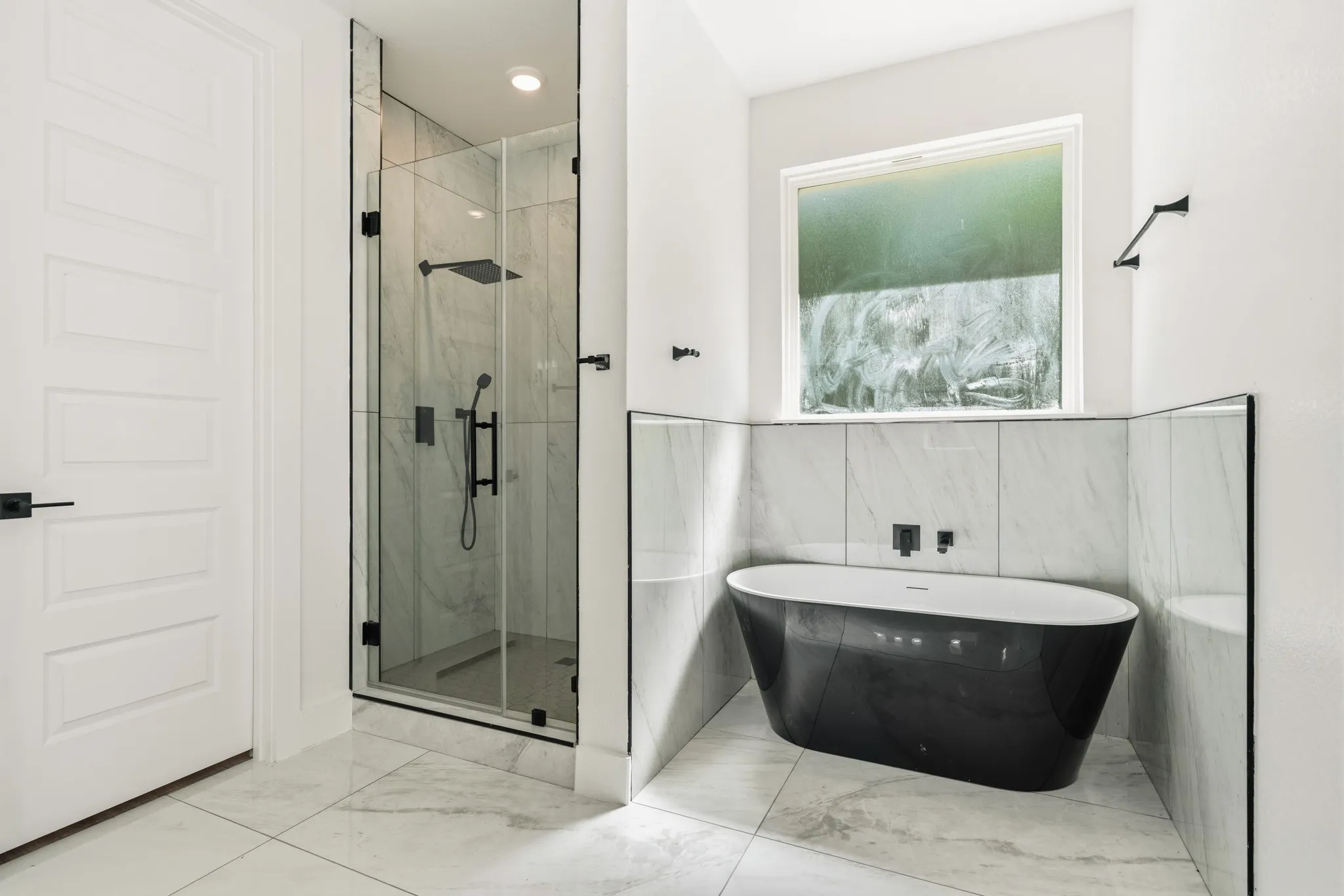 Modern bathroom featuring a freestanding black soaking tub, a frameless glass shower enclosure with matte black fixtures, and large-format tile flooring