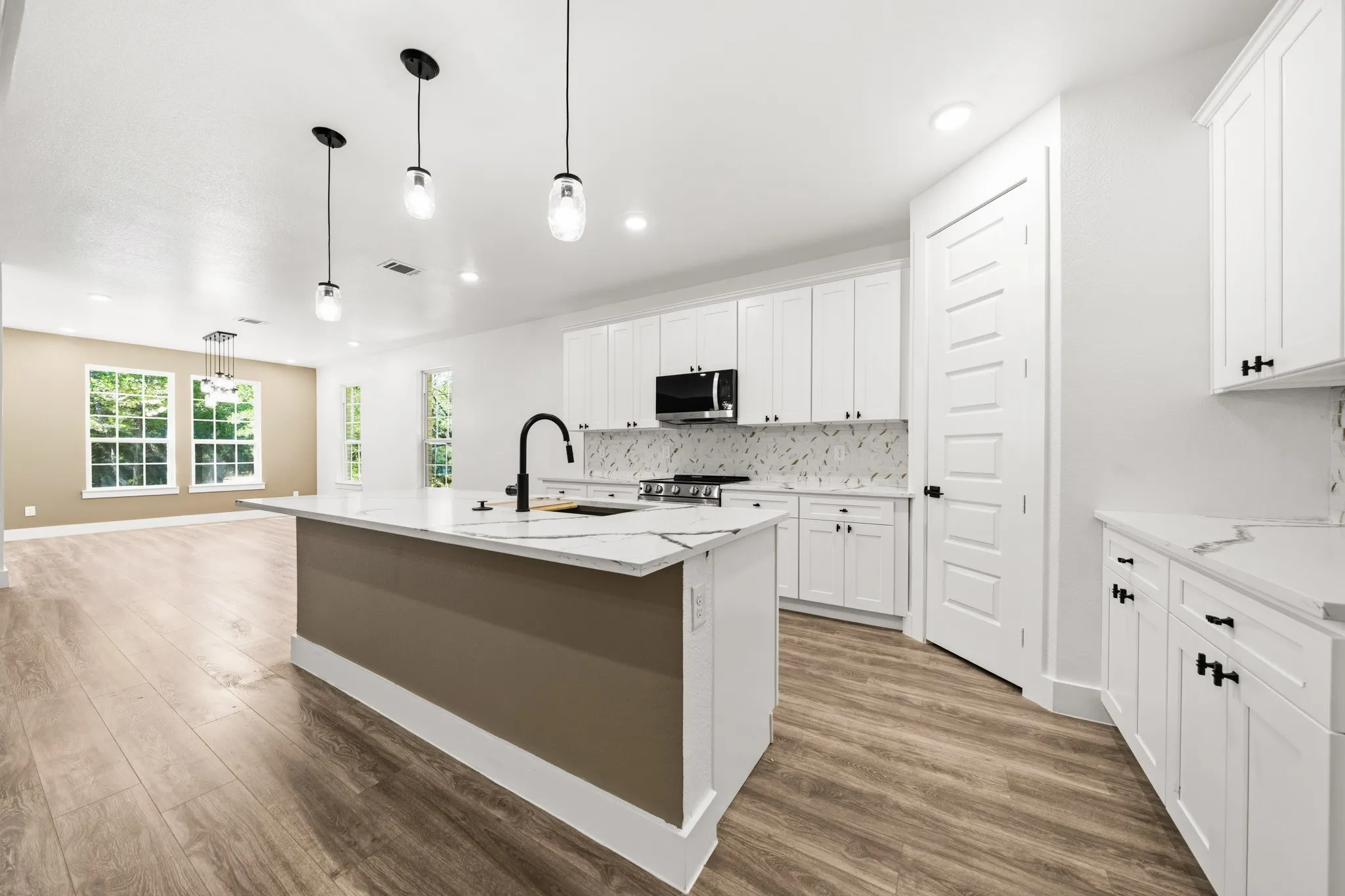 Open-concept kitchen featuring an expansive island with a matte black faucet, white shaker cabinetry with black hardware, and patterned stone countertops with a matching backsplash
