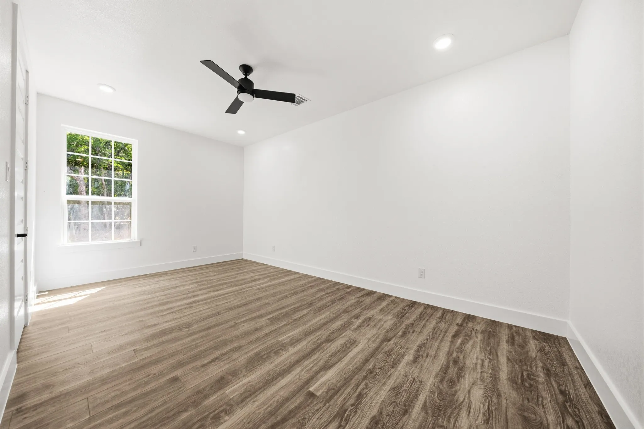 Spacious room featuring wood-finish flooring, recessed lighting, and a contemporary ceiling fan