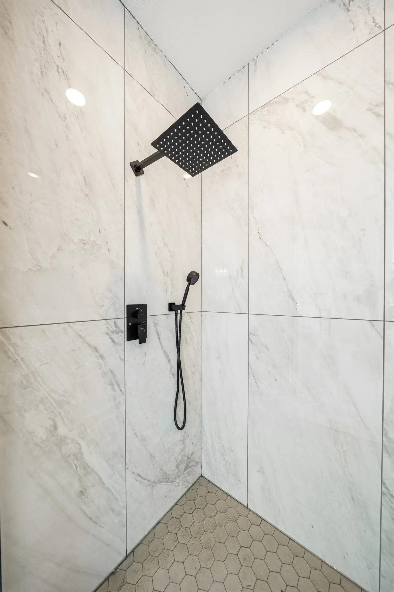 Shower with large format white tile walls, a matte black rainfall showerhead, and a matching matte black handheld shower fixture
