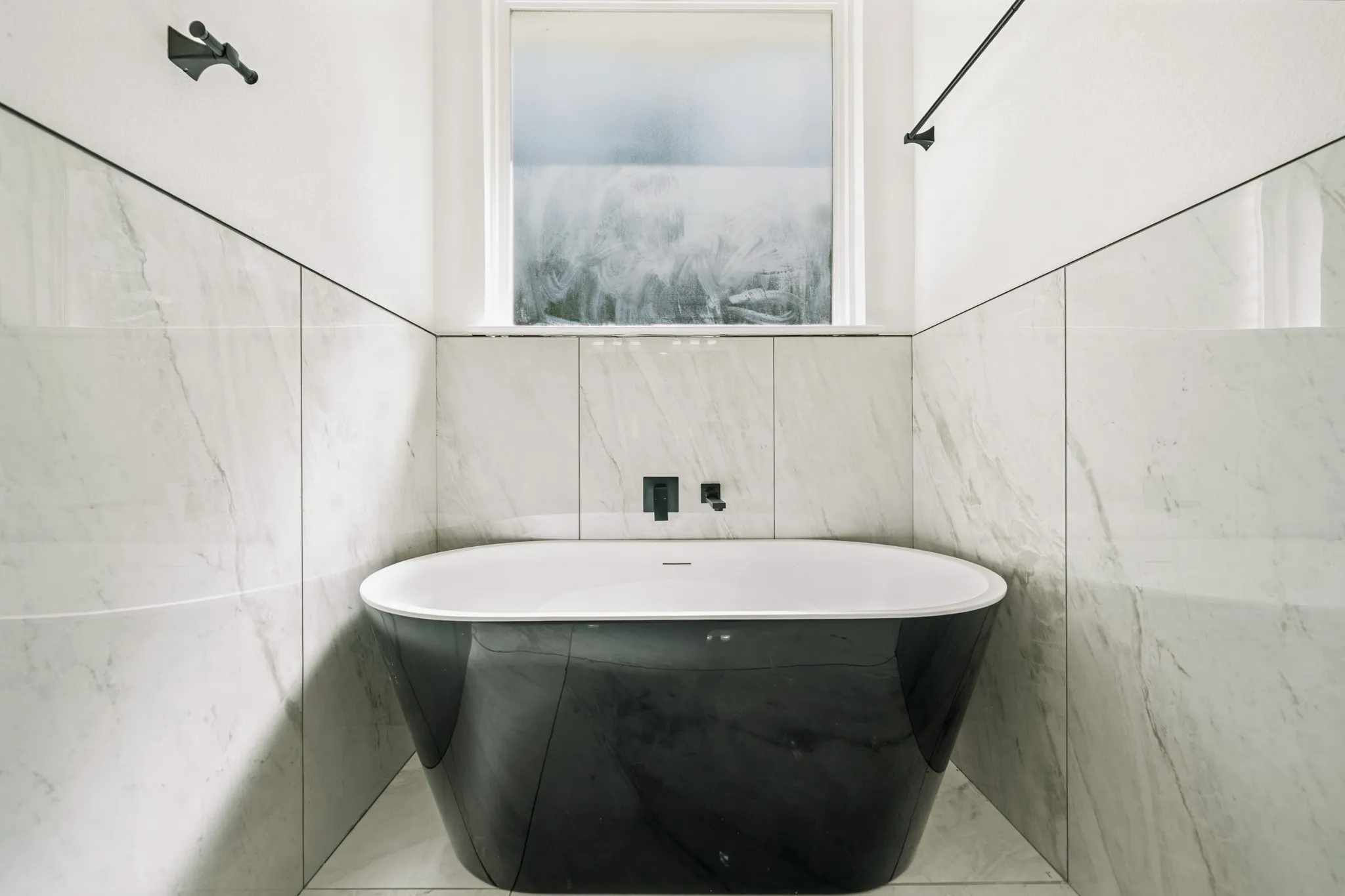 Freestanding black soaking tub with a wall-mounted matte black faucet