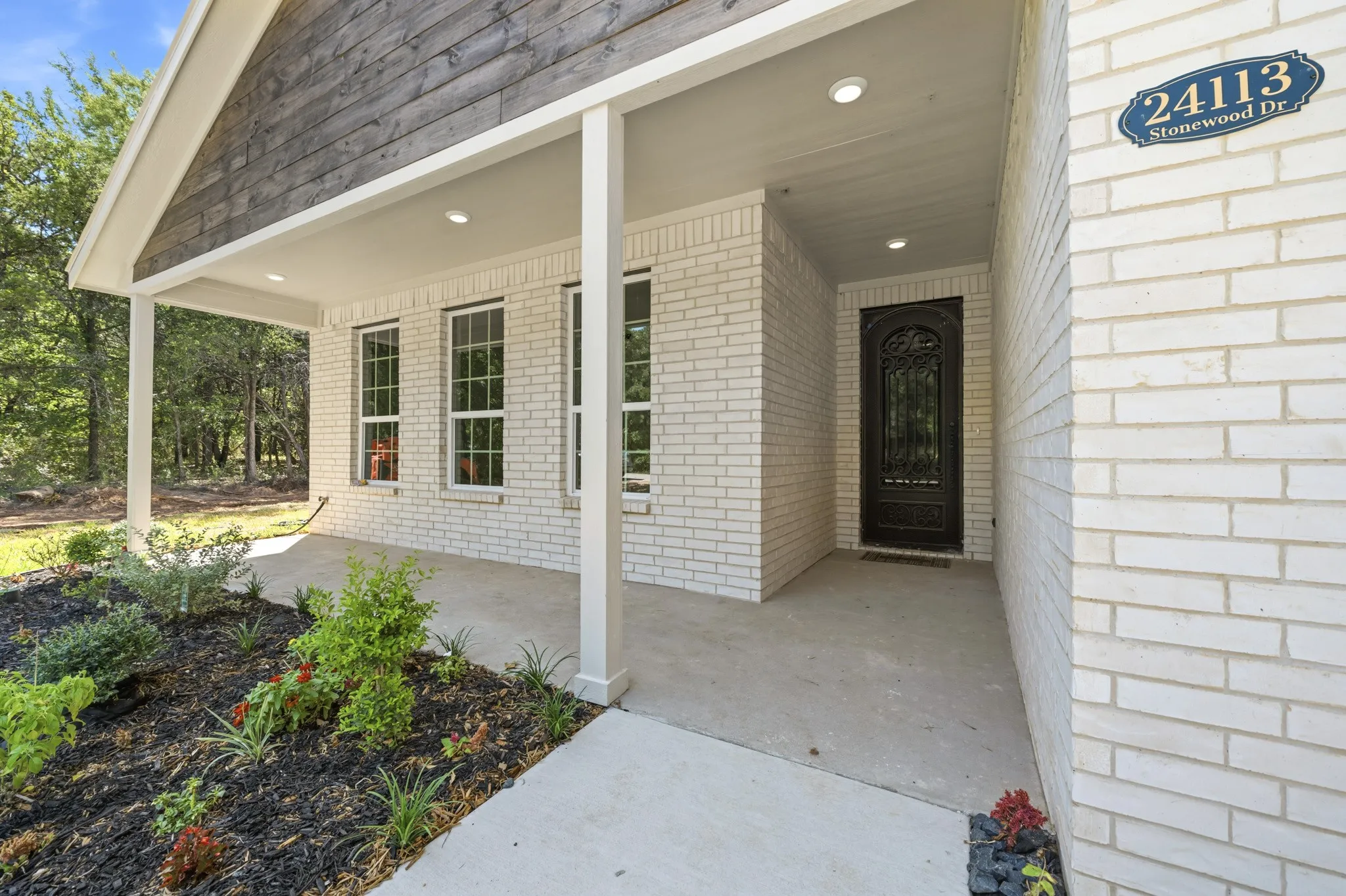 Charming front entry with a covered porch, white brick exterior, wood-paneled gable, and recessed lighting