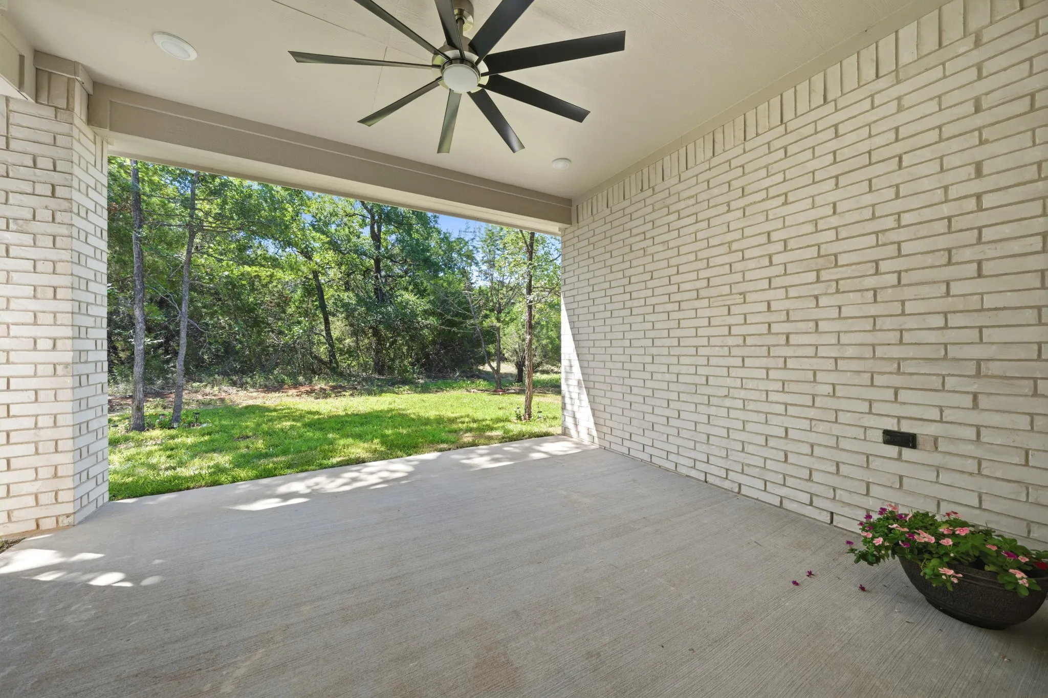 Covered patio featuring a concrete slab, white brick walls, a ceiling fan with dark blades, and recessed lighting