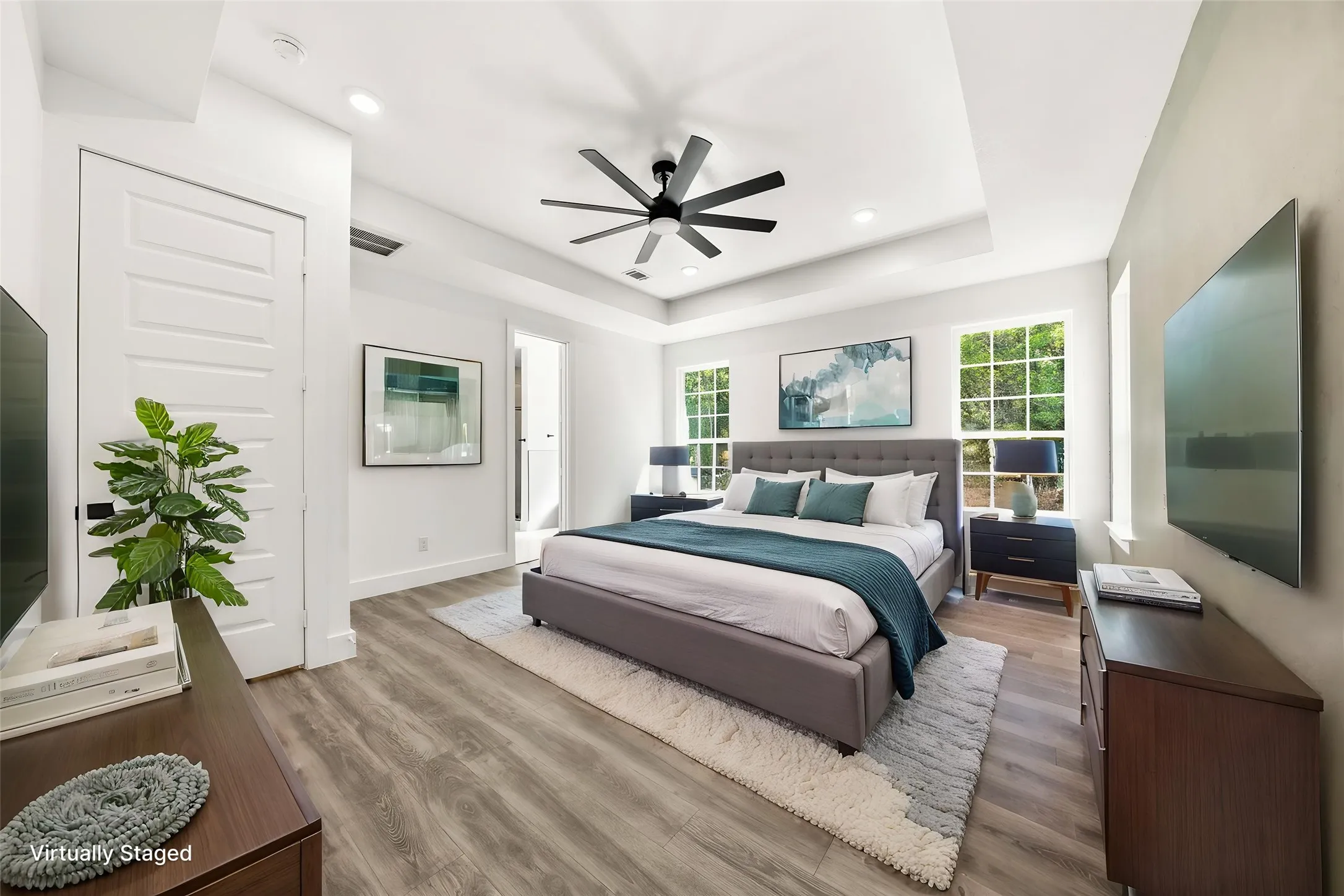 Spacious room featuring wood-finish flooring, a tray ceiling with a modern ceiling fan, recessed lighting, and multiple windows
