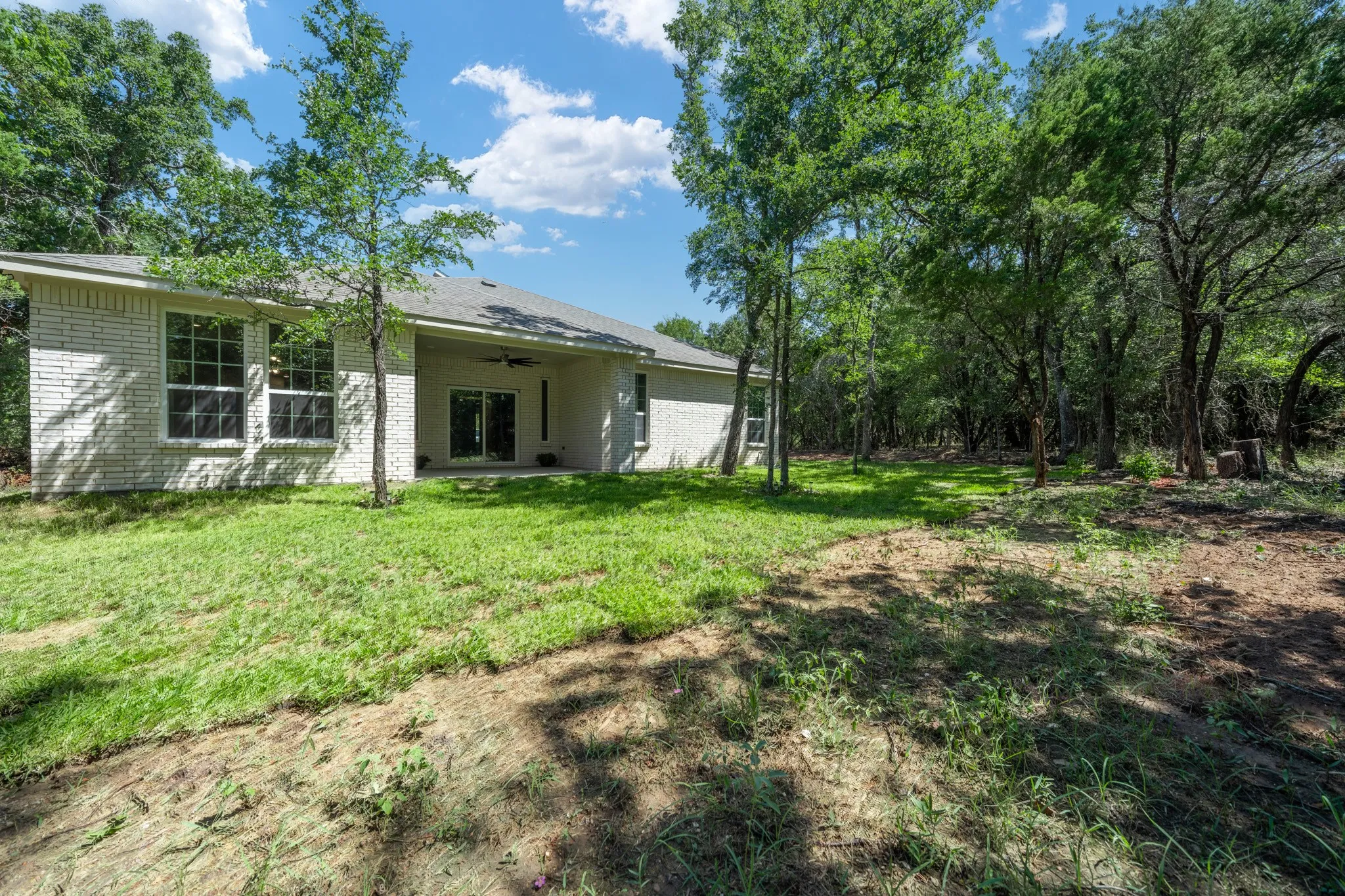 Rear exterior featuring a covered patio with ceiling fan, sliding glass door, and multiple windows