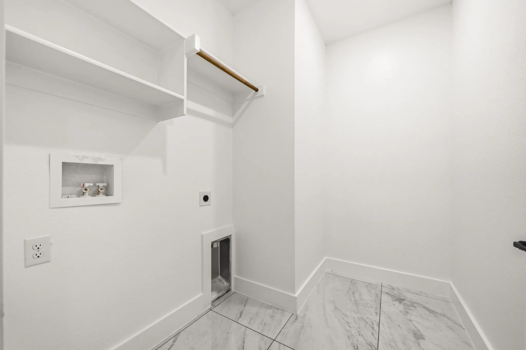Dedicated laundry area featuring white shelving, a wood garment rod, white baseboards, and light-toned marble-finish tile flooring