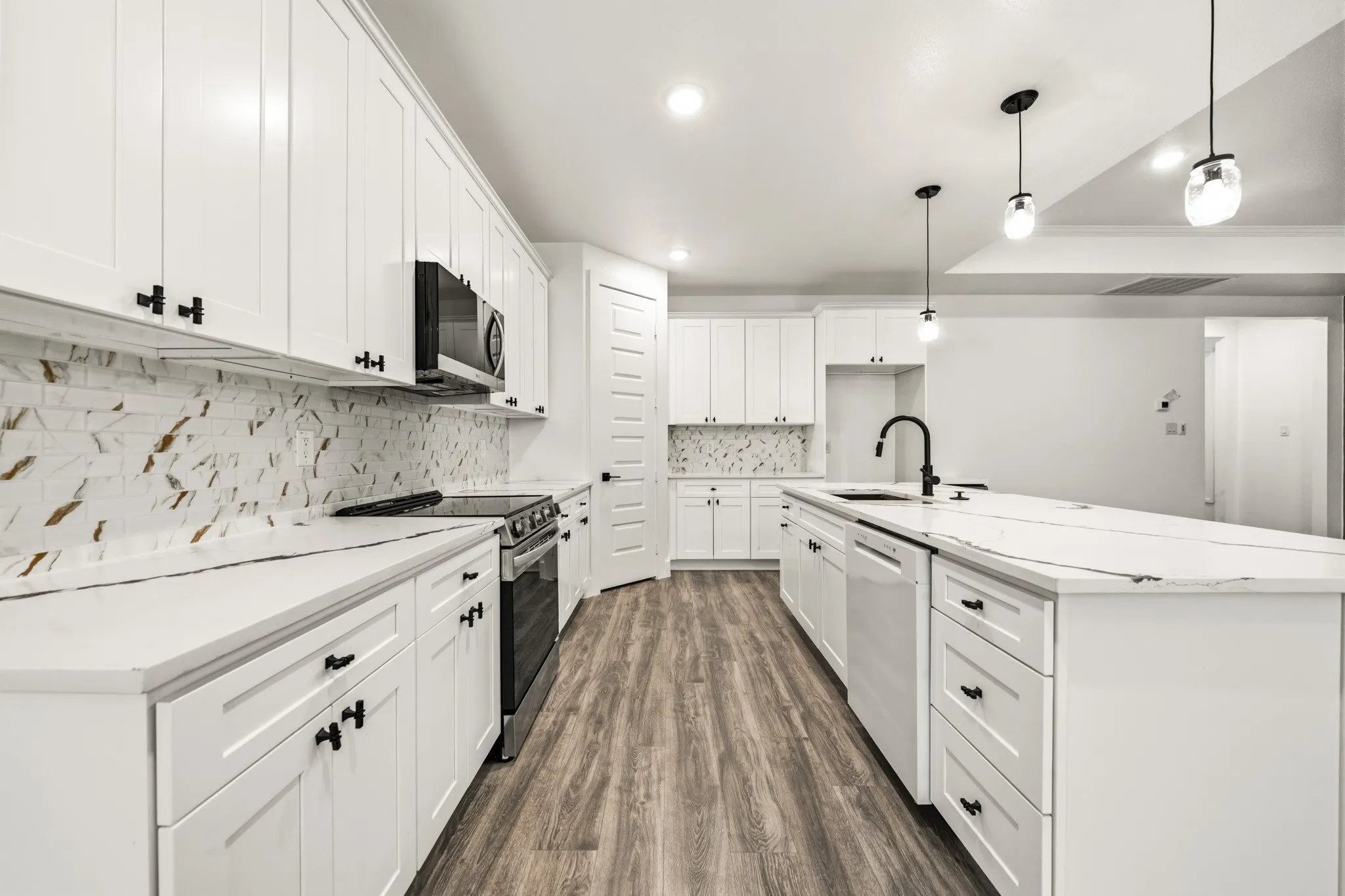Modern kitchen featuring white cabinetry with black hardware, a contrasting stone-look backsplash, wood-finish flooring, a center island with a black faucet, and pendant lighting