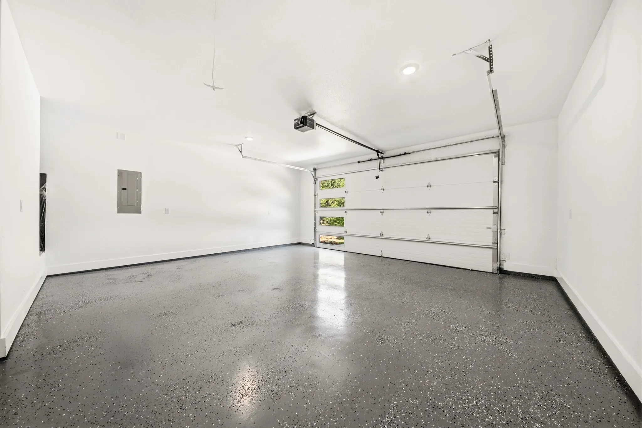 Spacious garage featuring a speckled epoxy floor, white painted walls, and a modern garage door with frosted glass panels