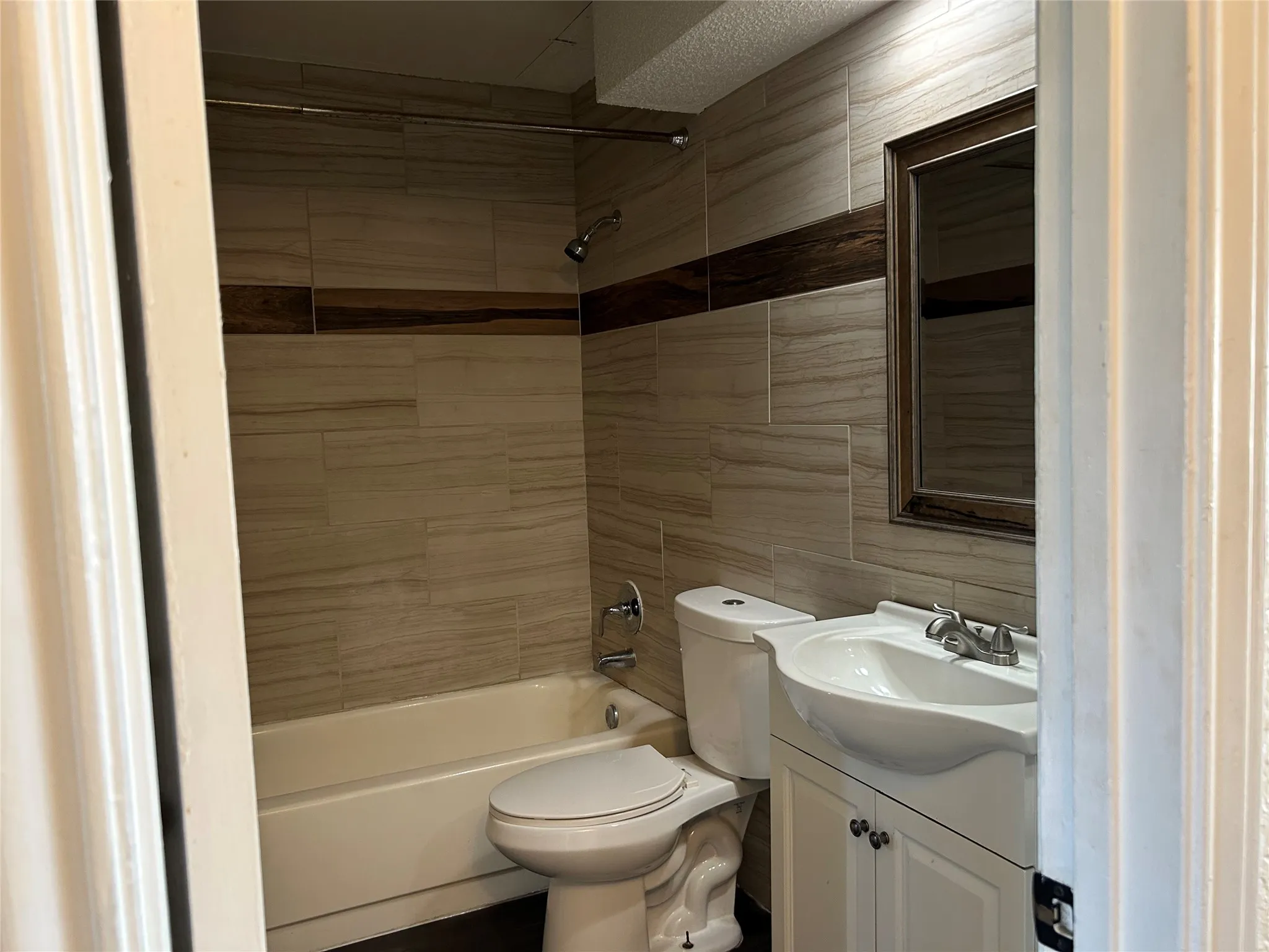 Bathroom featuring floor-to-ceiling tile, a full-size bathtub with shower, a modern vanity with a white basin sink, and a framed mirror