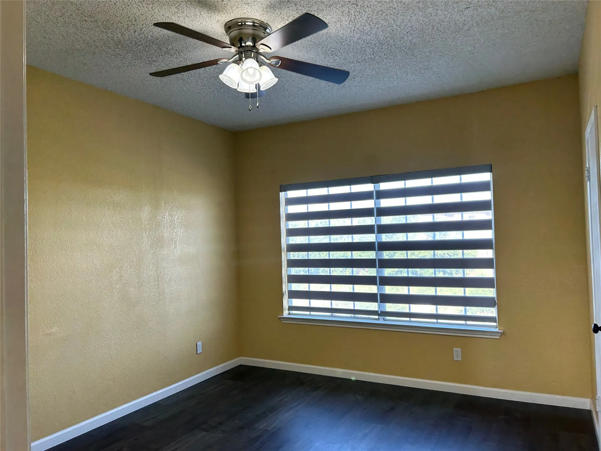 Room featuring wood-finish flooring, a window with horizontal blinds, and a ceiling fan with integrated lighting