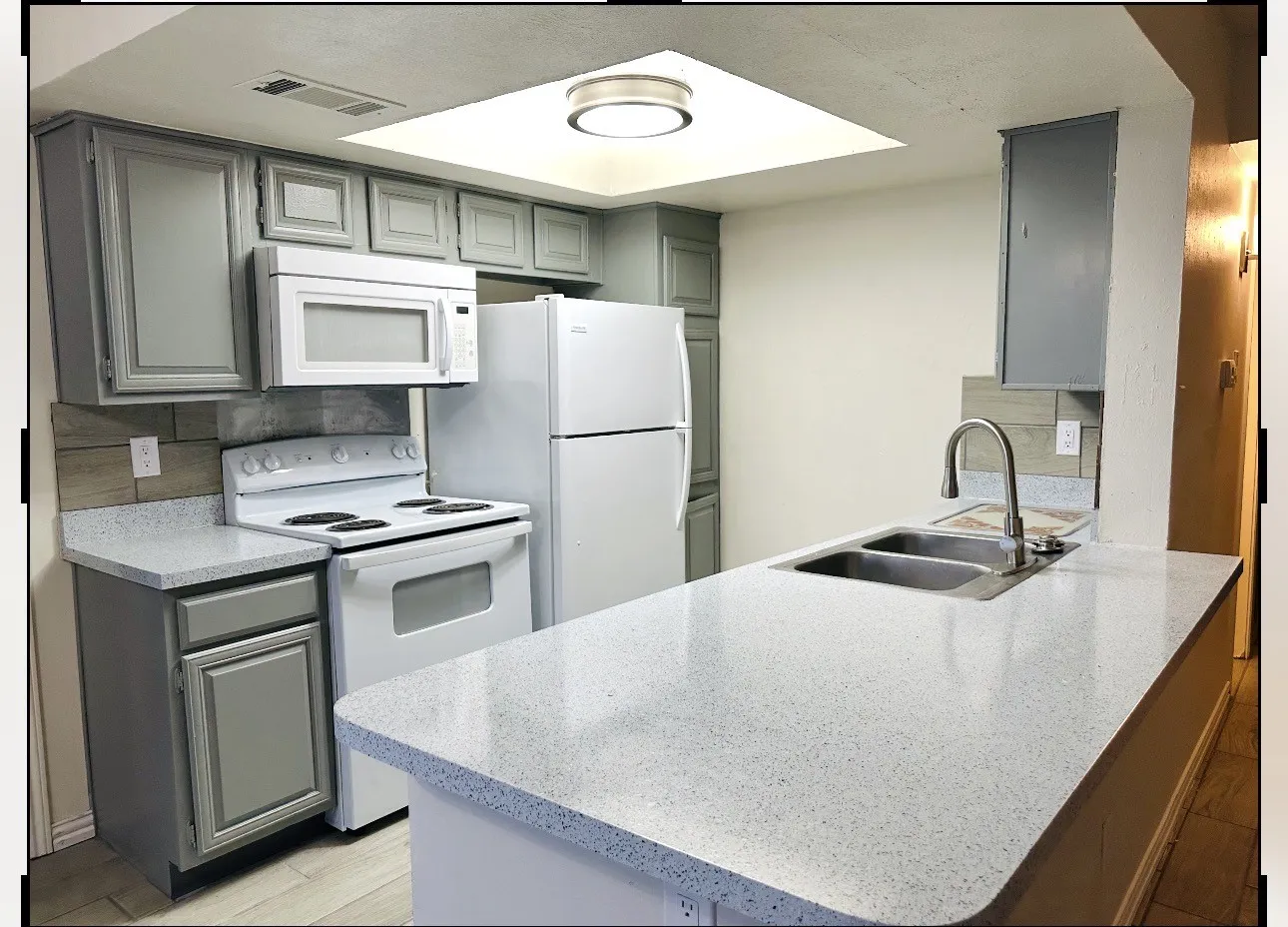 Kitchen featuring light gray cabinetry, speckled white countertops, a double basin stainless steel sink with a gooseneck faucet, a light wood-finish backsplash, and an overhead microwave