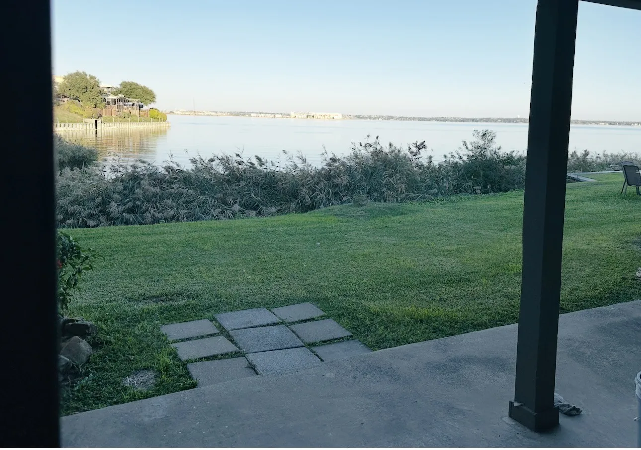 Waterfront backyard featuring a concrete patio, stepping stones, and a grass lawn extending to the water's edge