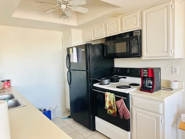 Kitchen featuring white cabinetry, a black appliance suite, light-toned countertops, and a ceiling fan with integrated lighting