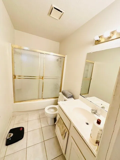 Bathroom featuring a tub with sliding shower doors, a single vanity with an integrated sink, a wall-mounted mirror, and tile flooring
