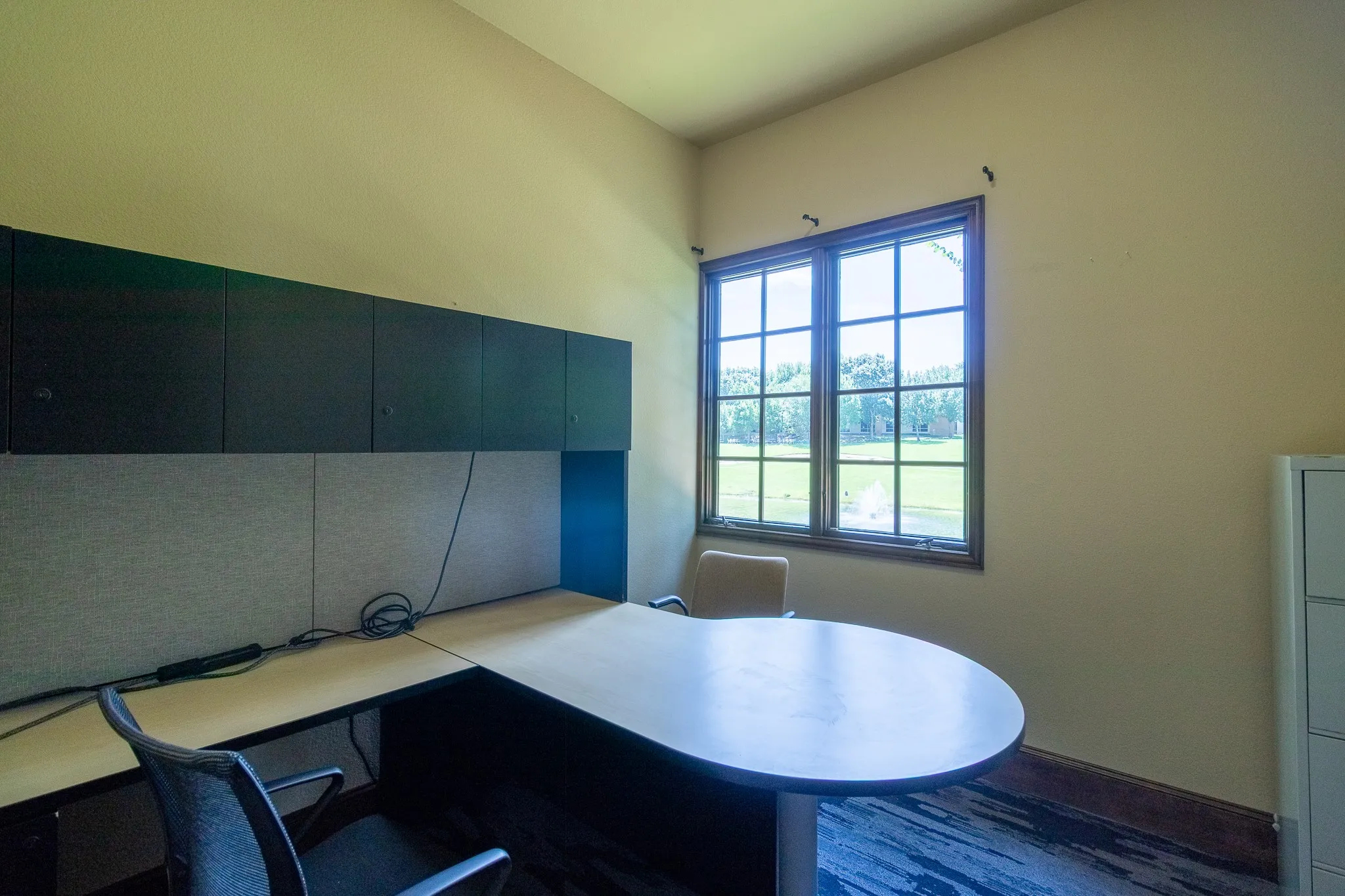 Office #2 space featuring a large window, built-in black cabinetry, an L-shaped desk, and wood-finish flooring