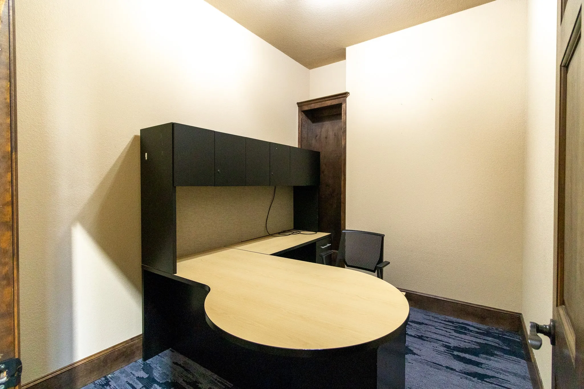 Dedicated room featuring an L-shaped built-in desk with overhead cabinetry, wood-finish baseboards, and a paneled door