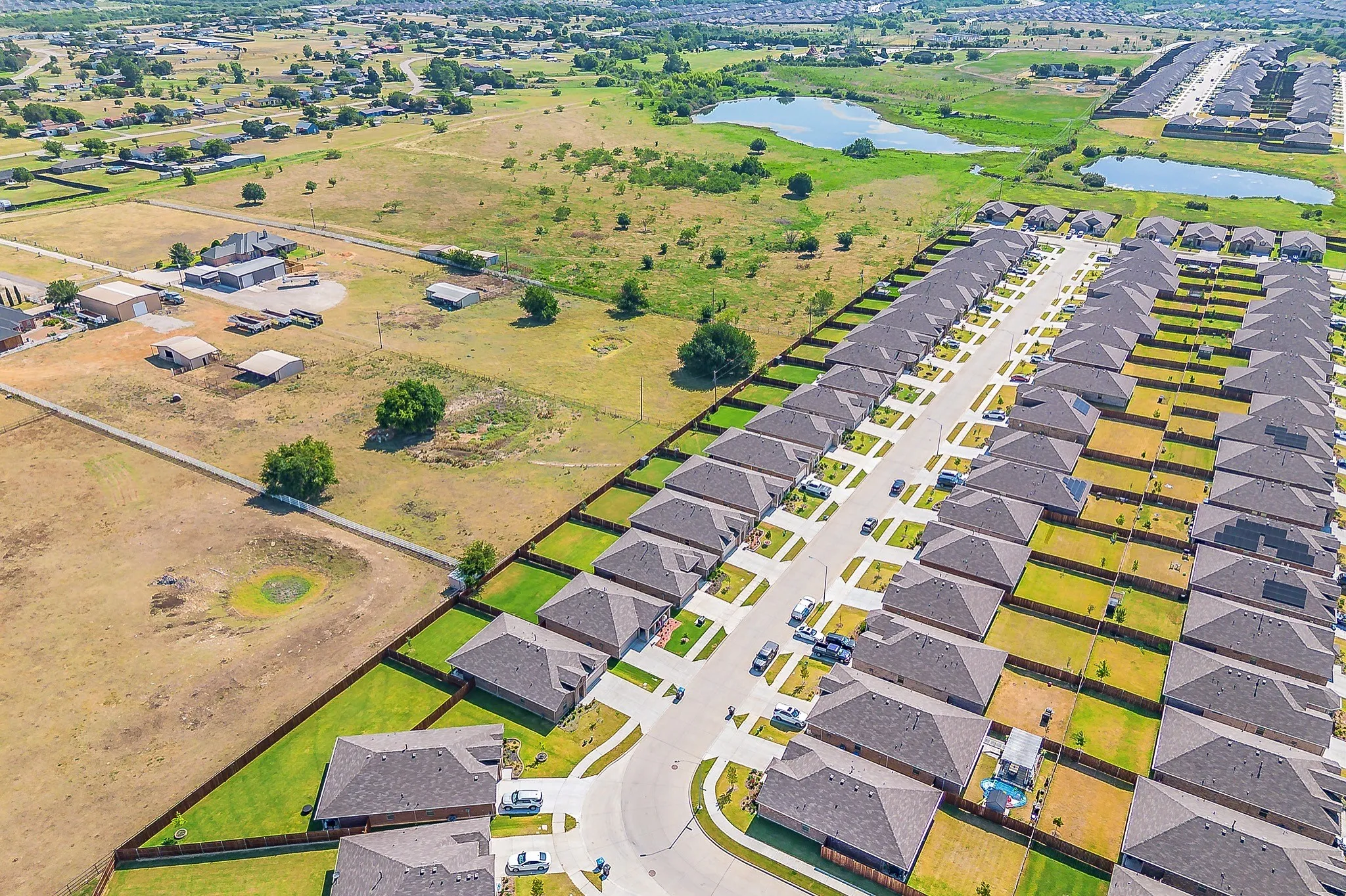 Aerial perspective showcasing a developed residential street with uniform homes featuring dark shingle roofs and green lawns