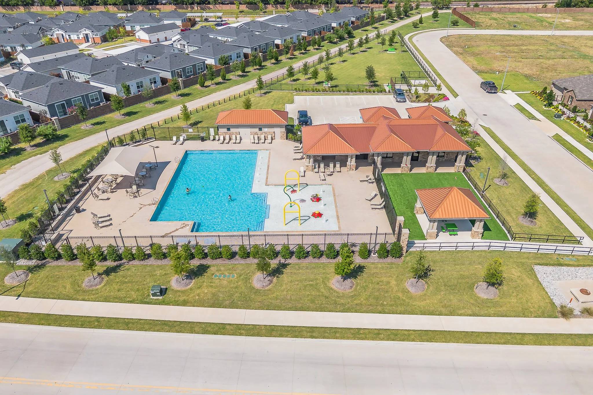 Community amenity center featuring a rectangular swimming pool, a children's splash pad, and a covered lounge area with a shade sail