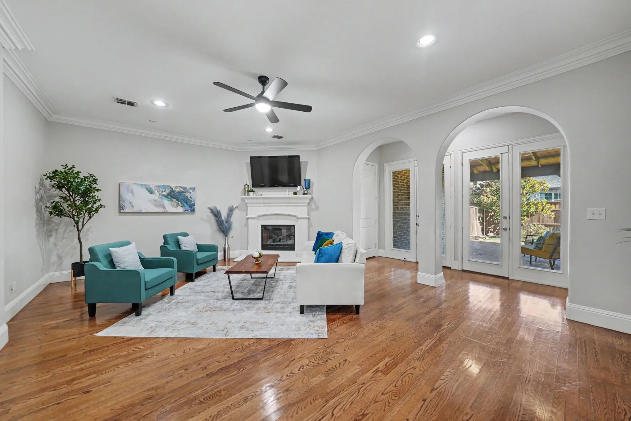 Hardwood flooring, recessed lighting, crown molding, white fireplace with mantle, and arched doorways