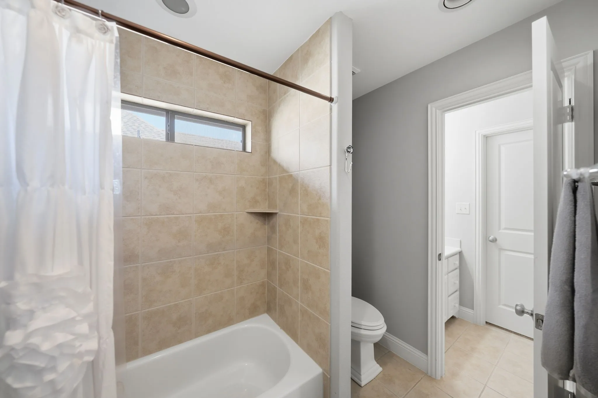 Bathroom featuring a tile-surround tub with built-in shelf, horizontal window, and recessed lighting