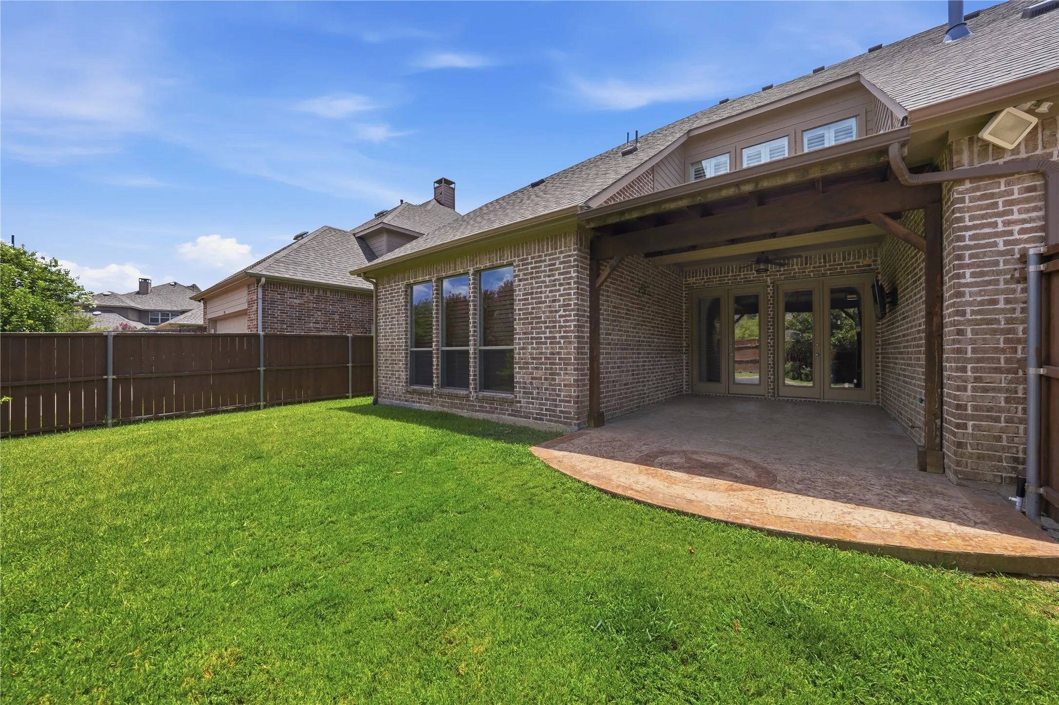 Expansive backyard featuring a covered patio with a stamped concrete surface, brick exterior, wood fence, and a manicured lawn