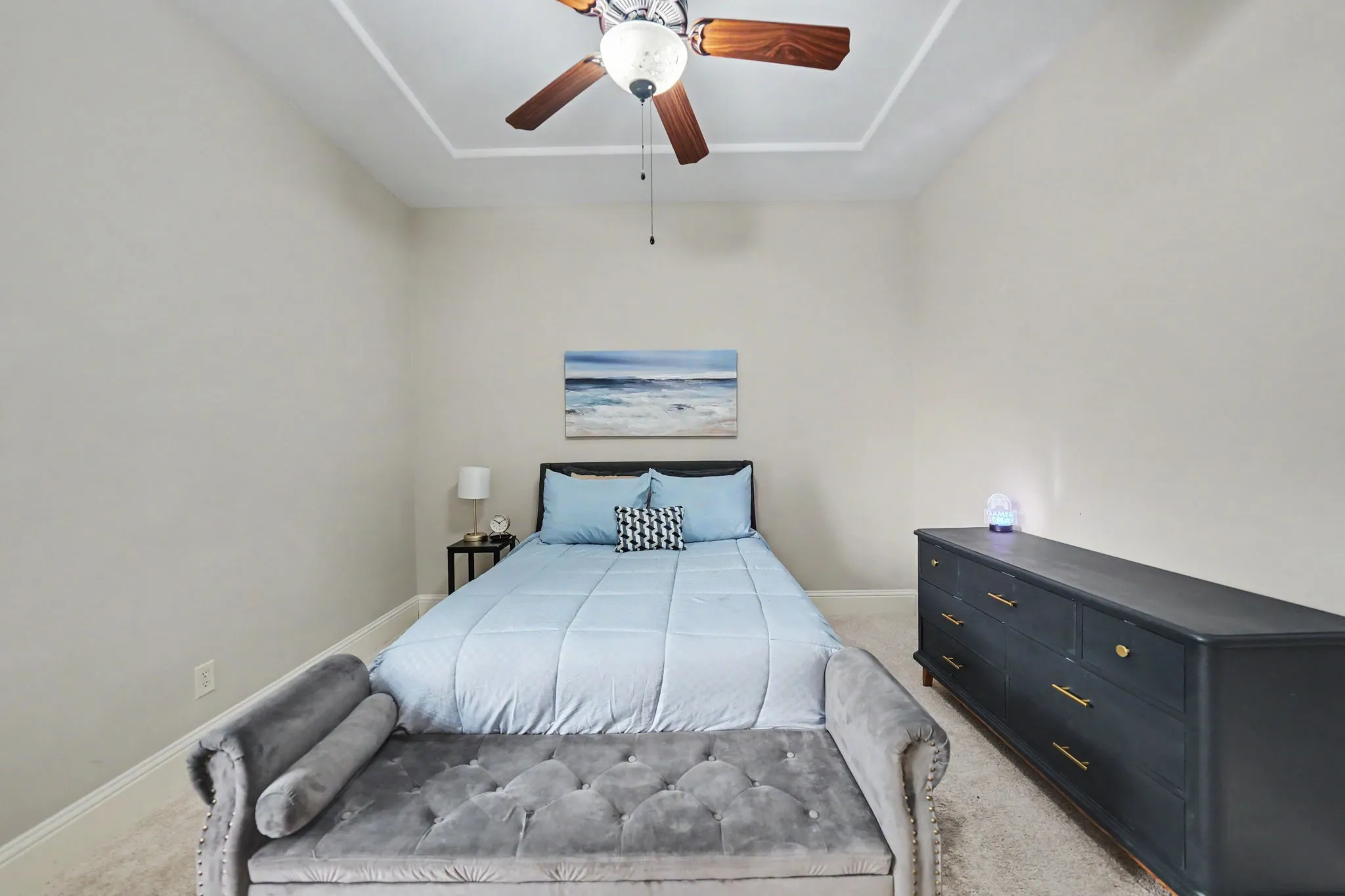 Tray ceiling with a ceiling fan light fixture, light-colored wall paint, and light-colored carpeting