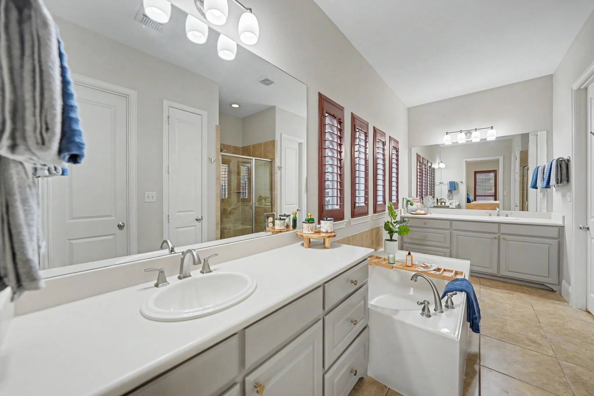 Dual vanities with undermount sinks, spacious countertop, built-in soaking tub, and tile flooring