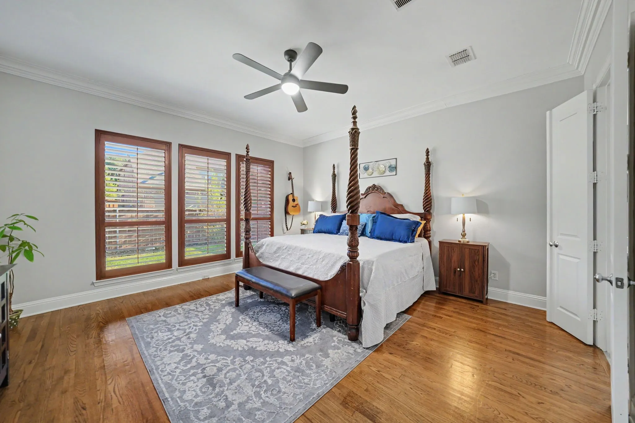 Hardwood flooring, crown molding, ceiling fan, three windows with wood blinds, and a paneled door