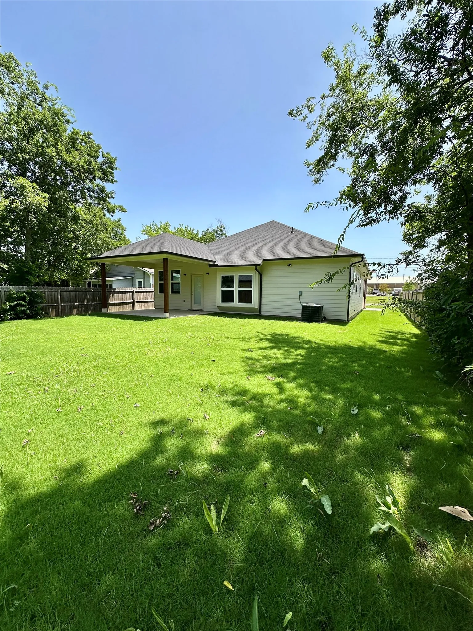 Expansive green lawn with a covered patio, featuring wood support columns and a dark shingle roof