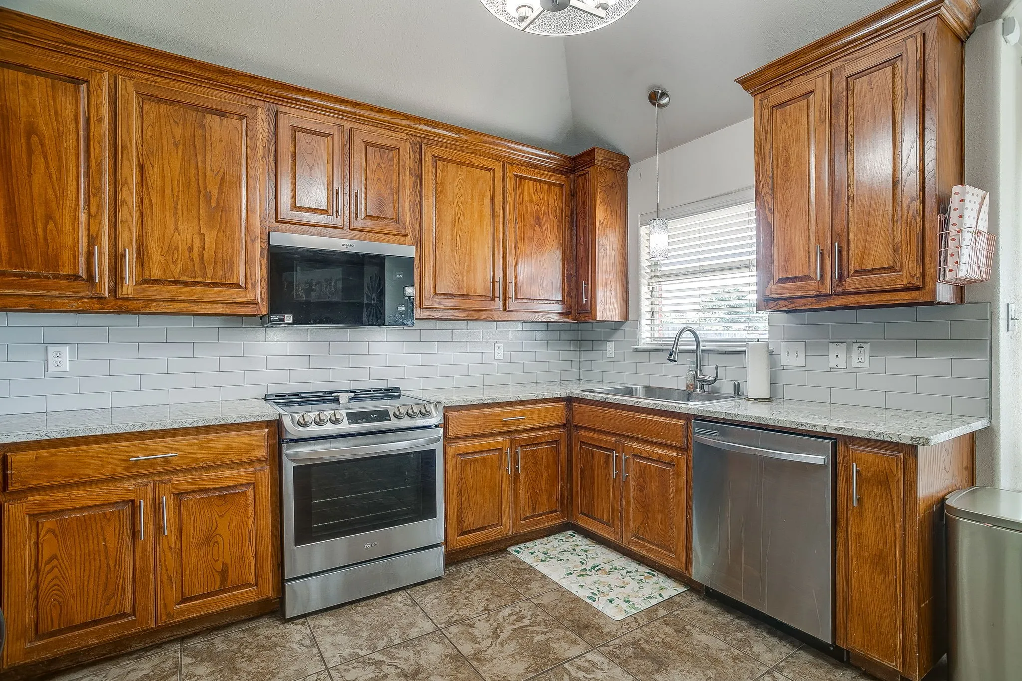 Kitchen featuring wood cabinetry, stainless steel appliances, granite countertops, and a subway tile backsplash