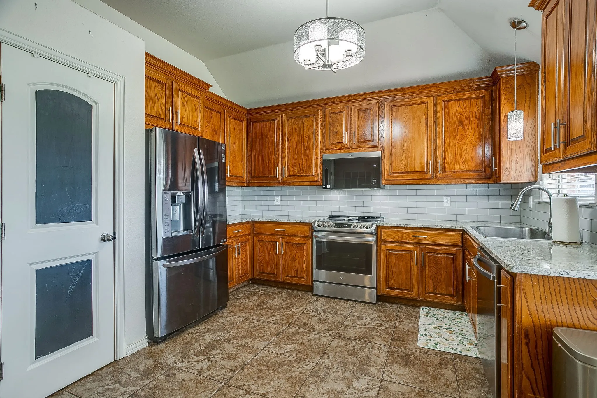 Kitchen featuring rich wood cabinetry, stainless steel appliances, light-toned countertops, white subway tile backsplash, and a contemporary ceiling light fixture