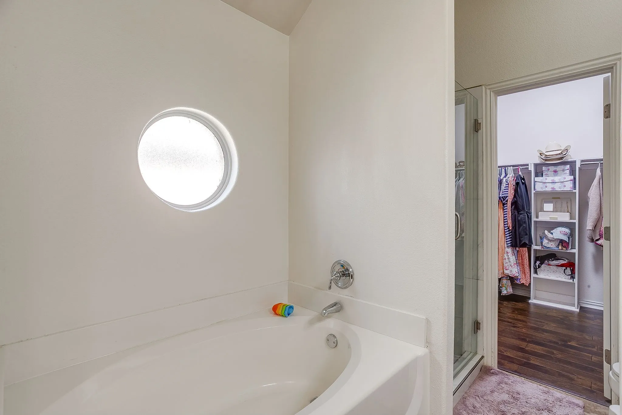 Bathroom with a circular frosted window, a built-in bathtub, and chrome fixtures