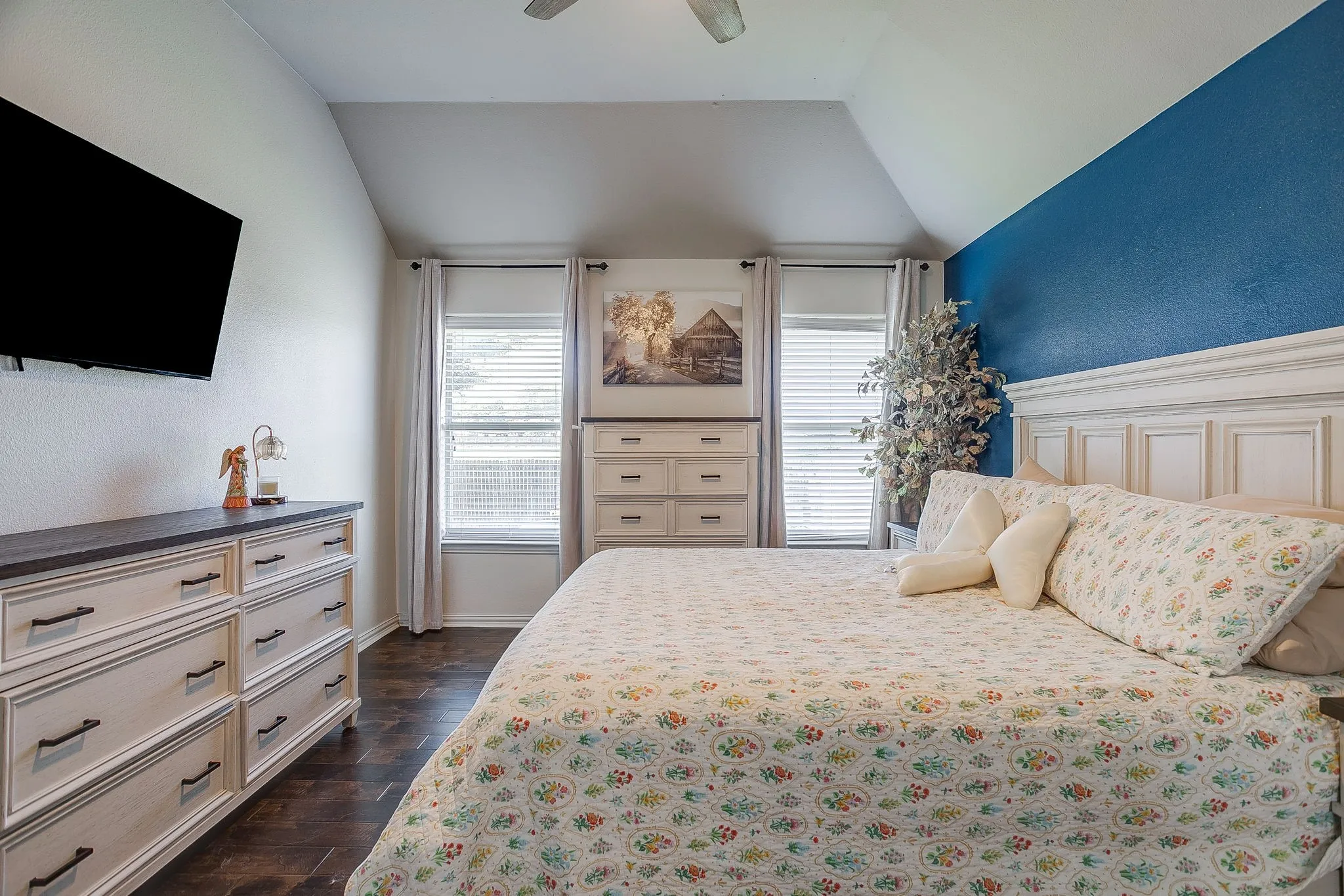 Vaulted ceiling room featuring wood-finish flooring, multiple windows with blinds, and a built-in wall-mounted television