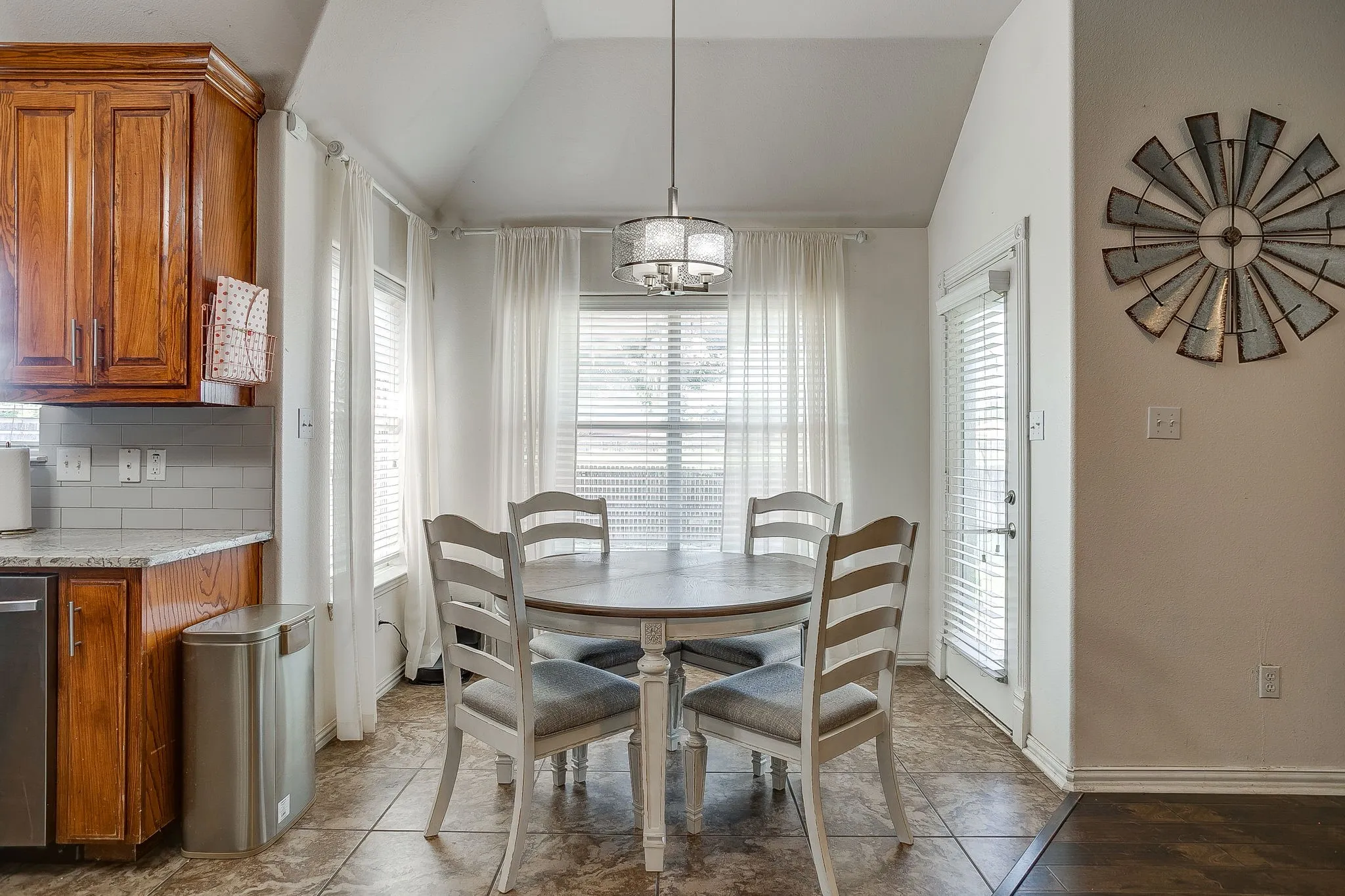 Dining area featuring vaulted ceilings, a contemporary chandelier, multiple windows with blinds and sheer curtains, and tile flooring