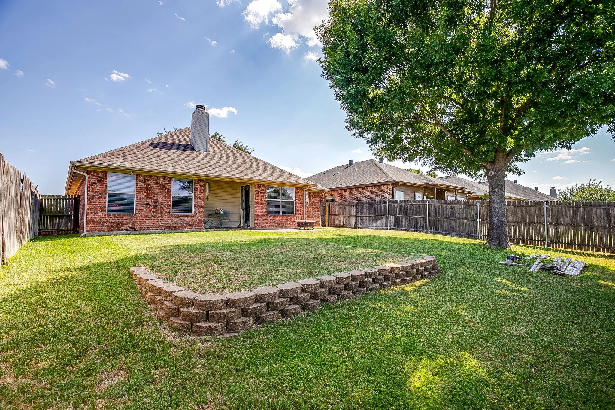 Spacious backyard featuring a brick retaining wall and mature tree