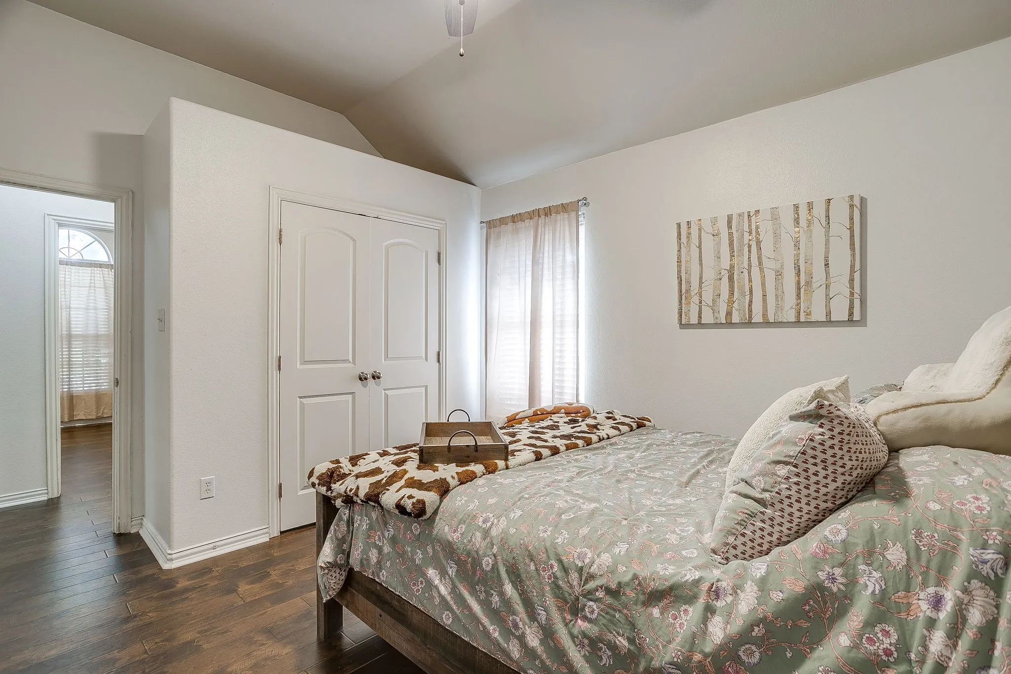 Bedroom featuring wood-finish flooring, white walls, and a window with blinds and sheer curtains