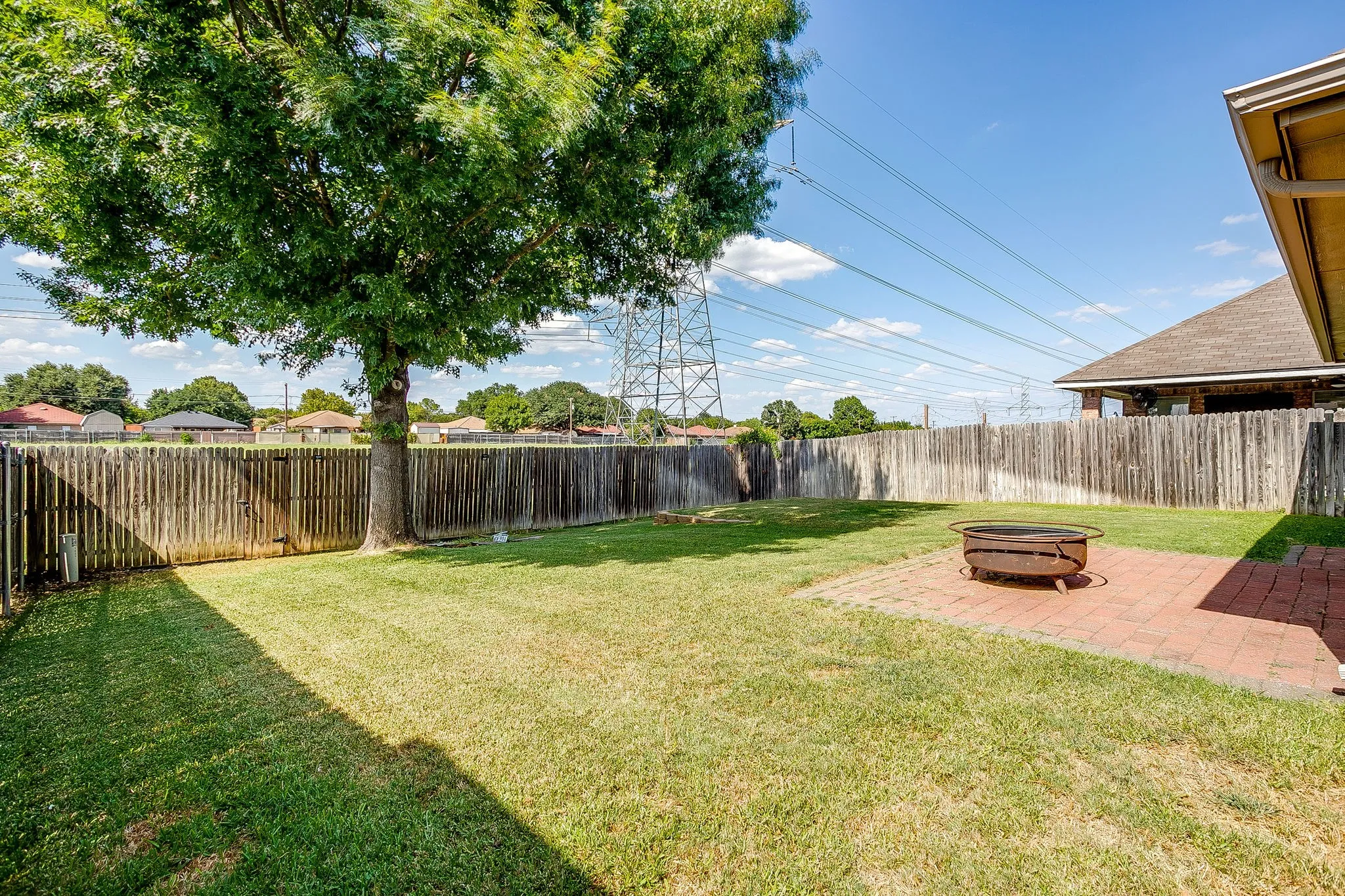 Spacious backyard featuring a manicured lawn, a mature shade tree, a wood privacy fence, and a brick paver patio