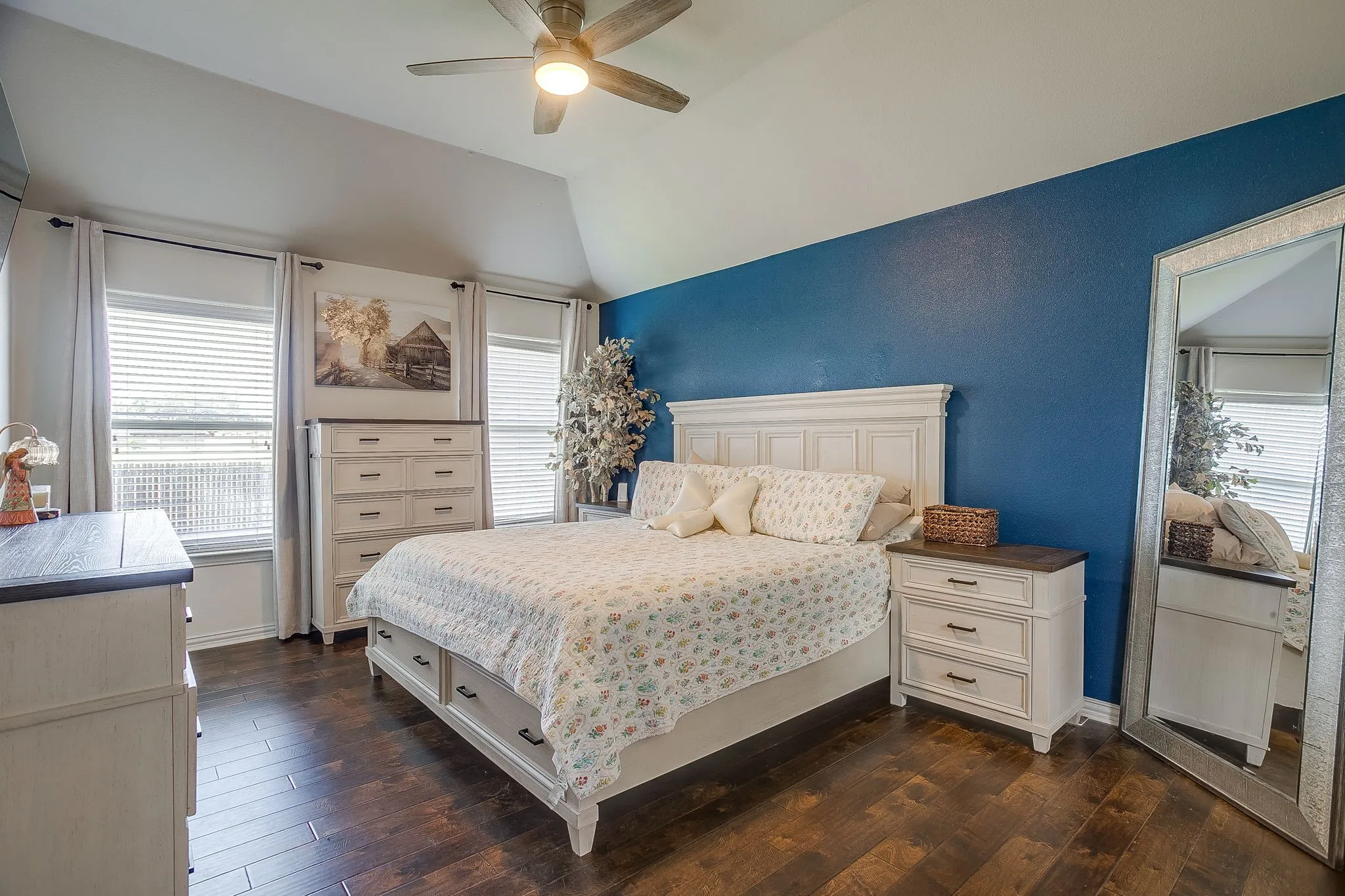 Room featuring vaulted ceilings, wood-finish flooring, a ceiling fan with integrated lighting, and multiple windows with blinds