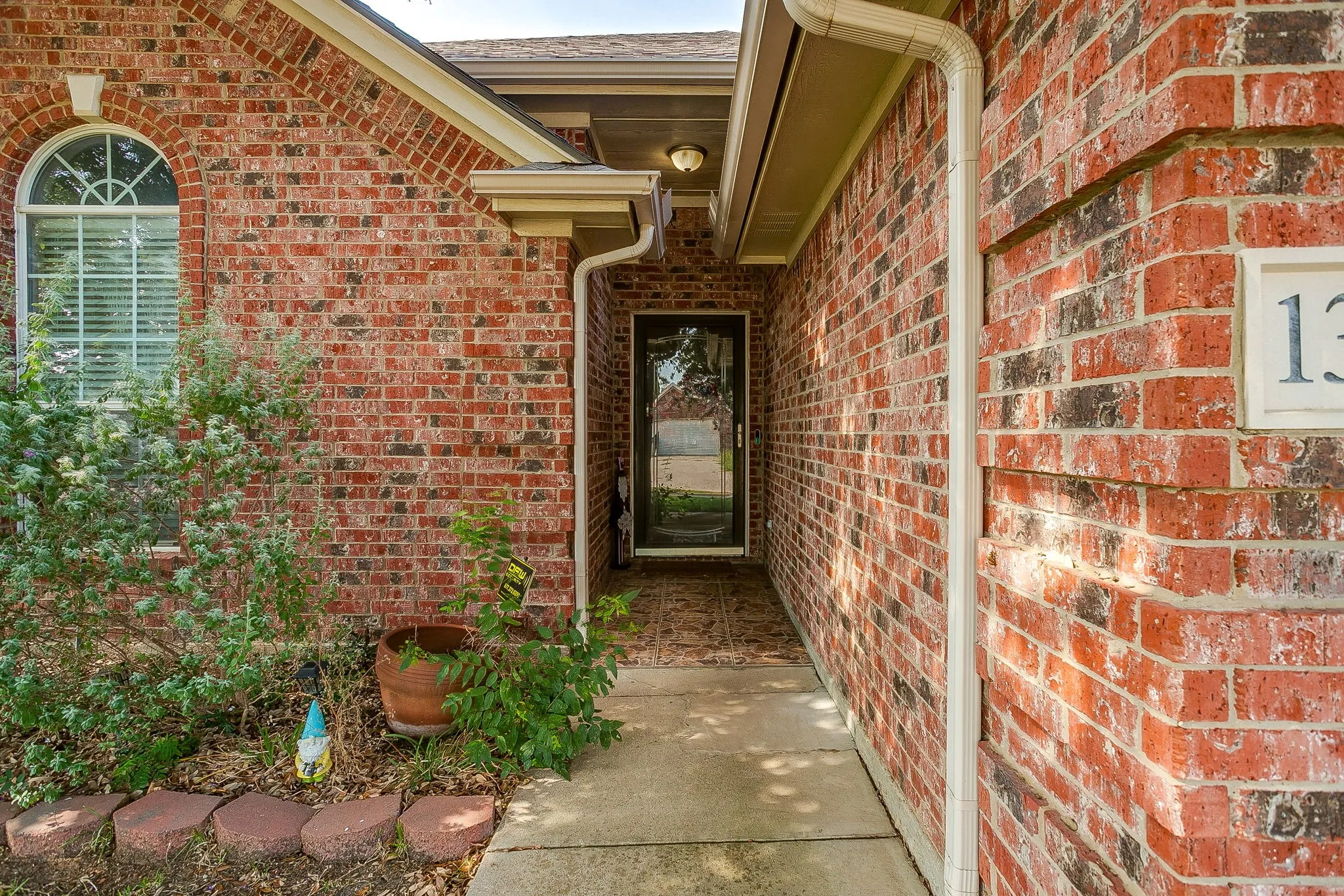 Brick exterior with a covered entry, arched window with horizontal blinds, and a concrete pathway