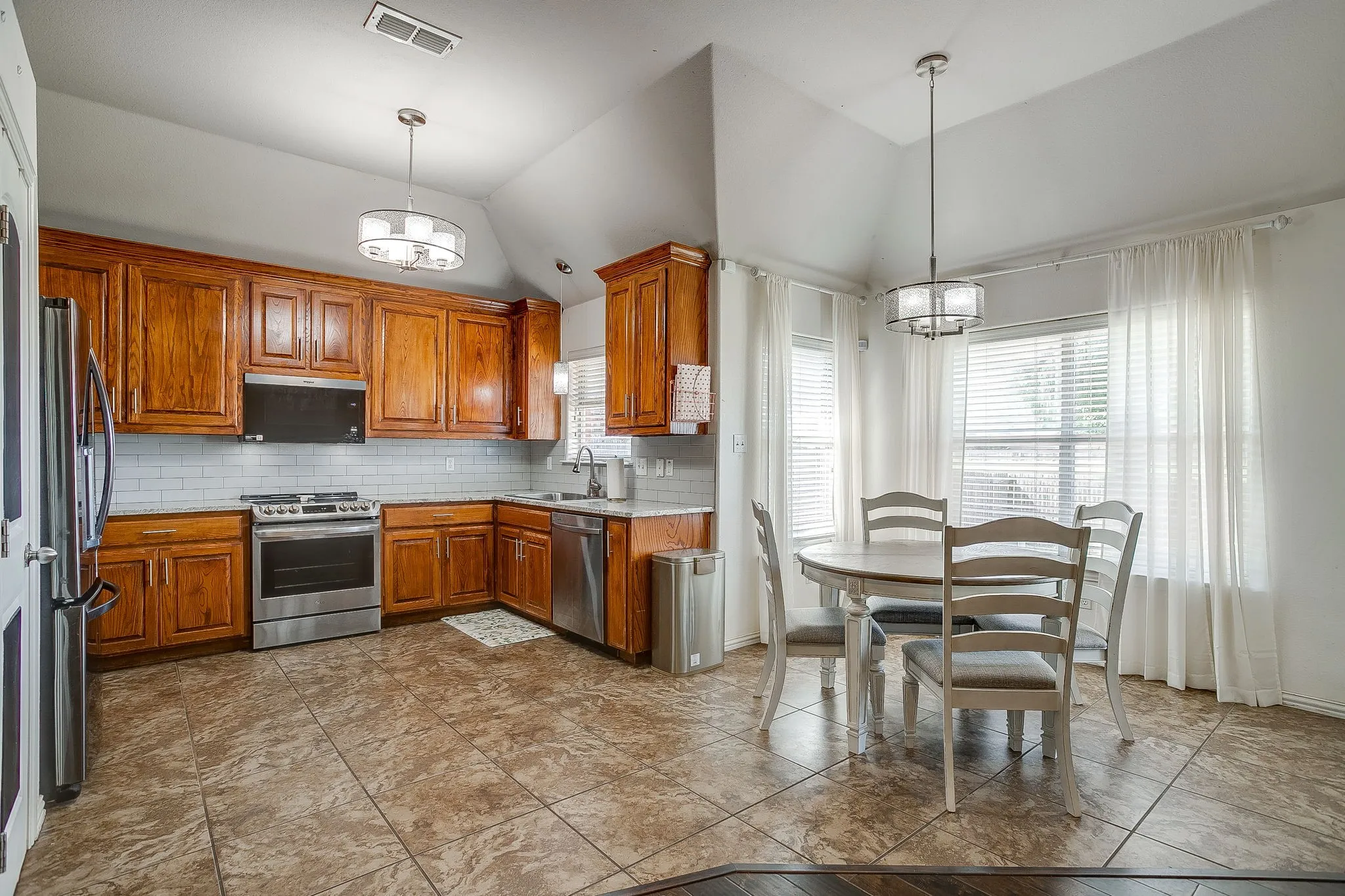 Kitchen featuring wood cabinetry, stainless steel appliances, white subway tile backsplash, and ceramic tile flooring