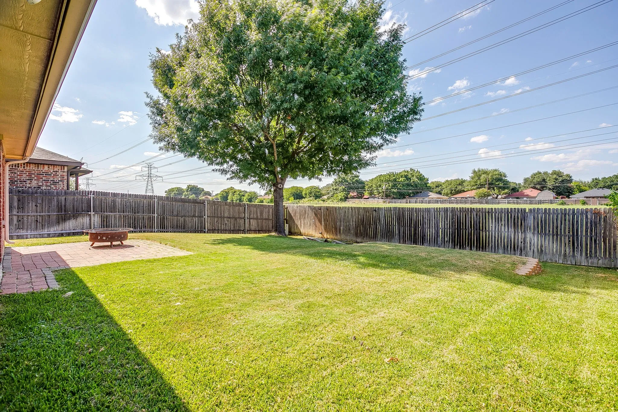 Expansive backyard featuring a brick paver patio, a mature shade tree, and a wooden privacy fence